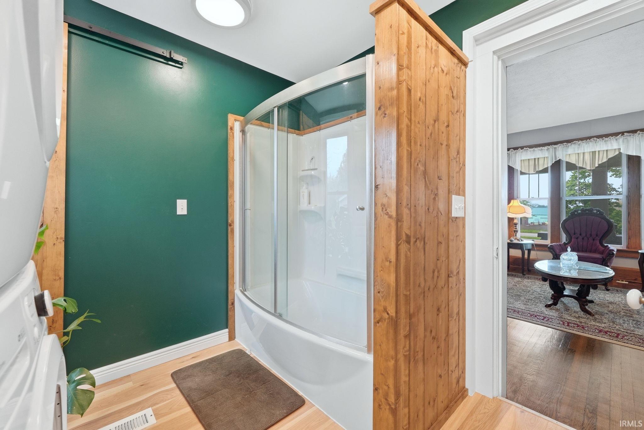 Three-quarter bathroom featuring a curved glass-enclosed shower, wood-finish flooring, dark green accent wall, and wood-paneled partition