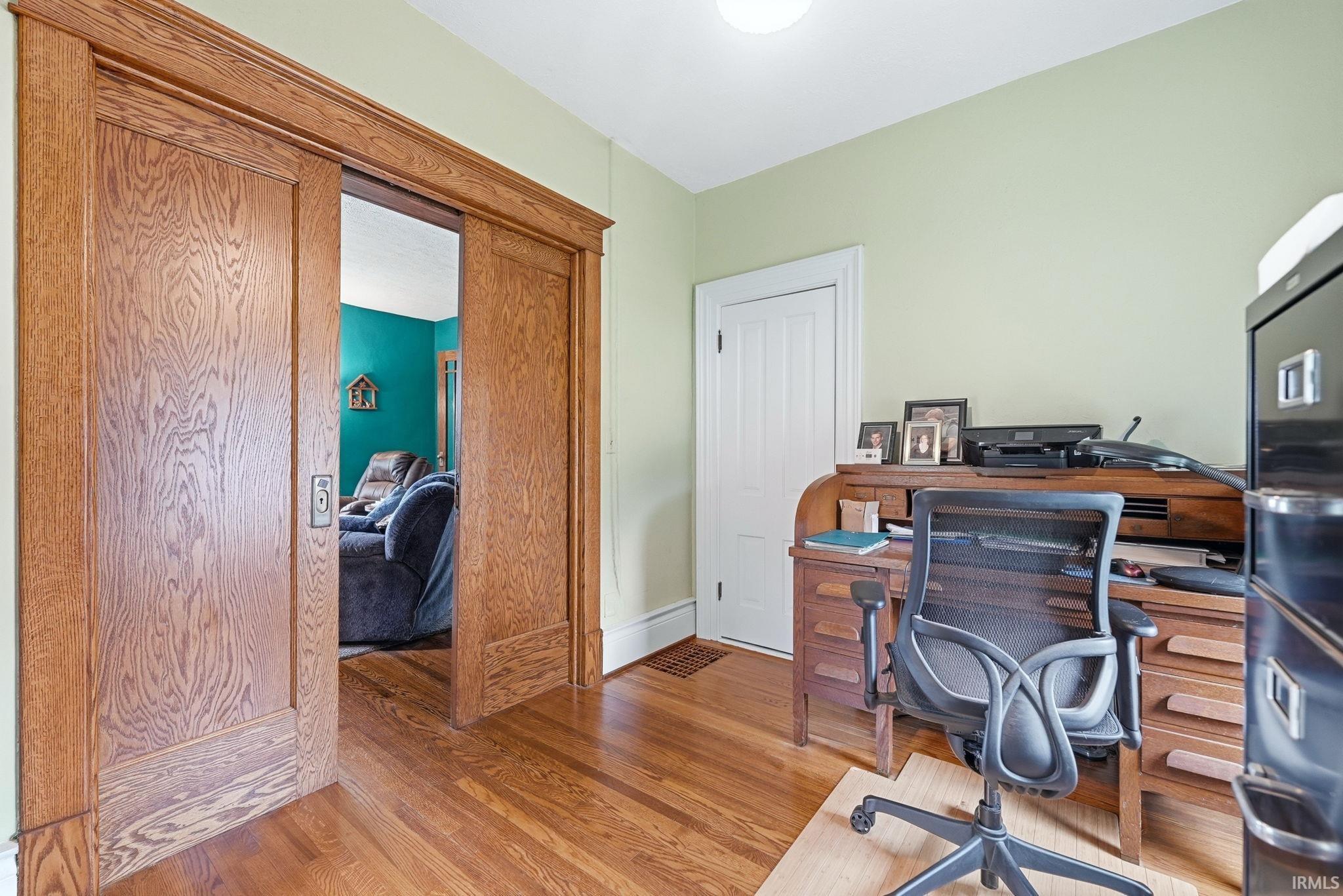 Hardwood flooring throughout featuring solid wood pocket doors with detailed trim work, a built-in secretary desk, and a painted paneled door