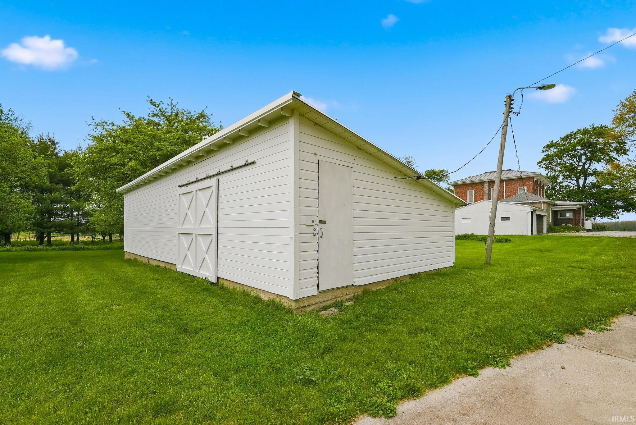 Detached outbuilding with white siding, a barn door, and a standard entry door, set on a concrete foundation