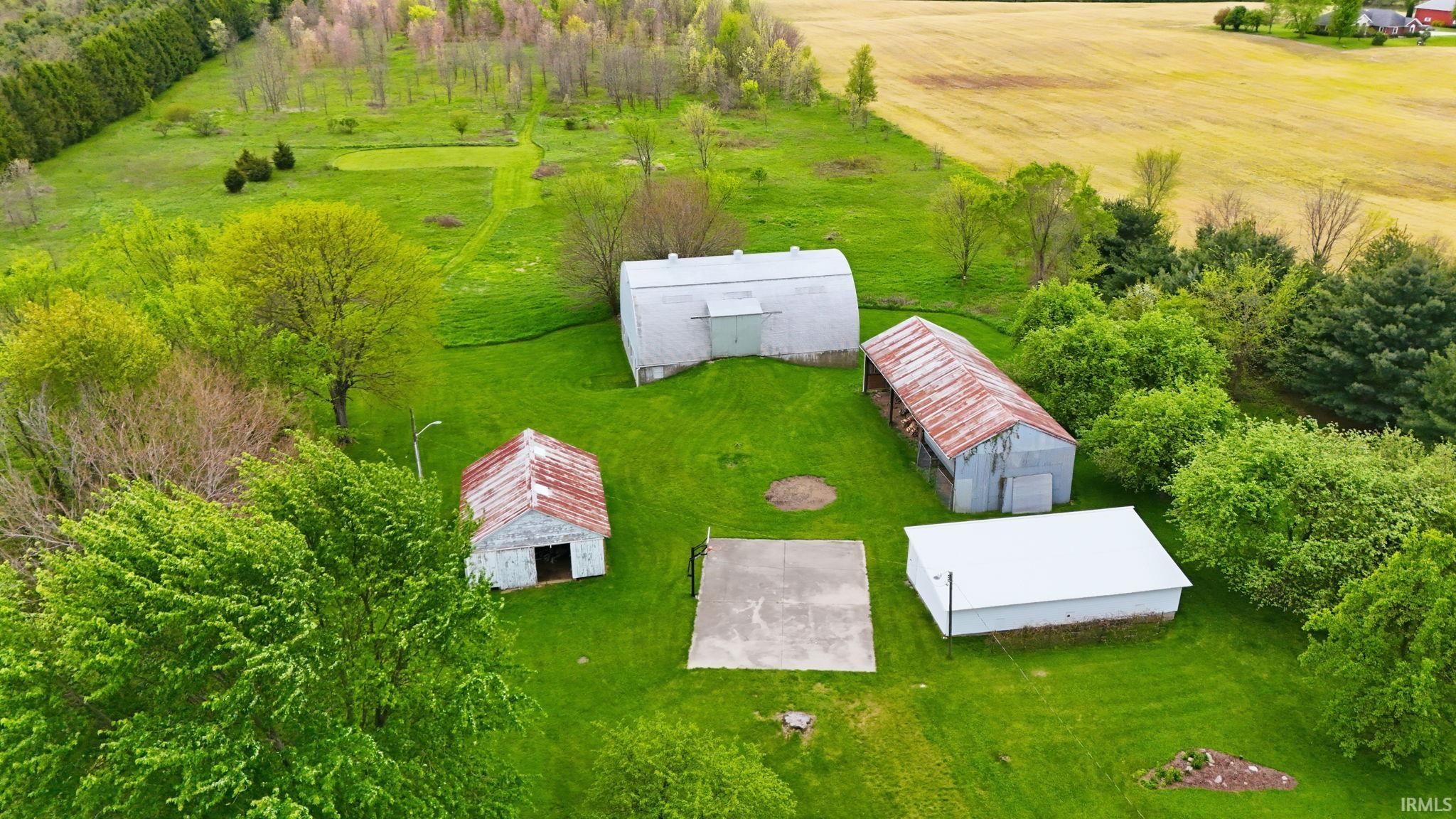 Expansive green landscape featuring multiple outbuildings, mature trees, a concrete pad, and distant agricultural fields