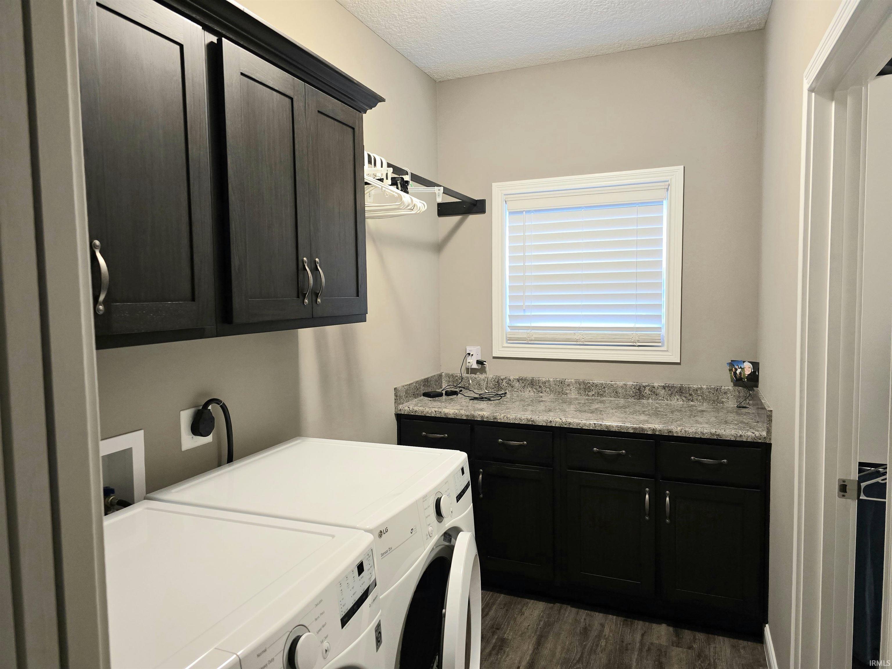 Laundry room featuring dark wood-finish cabinetry, a light-colored speckled countertop, a built-in hanging rack, and LVP flooring.
