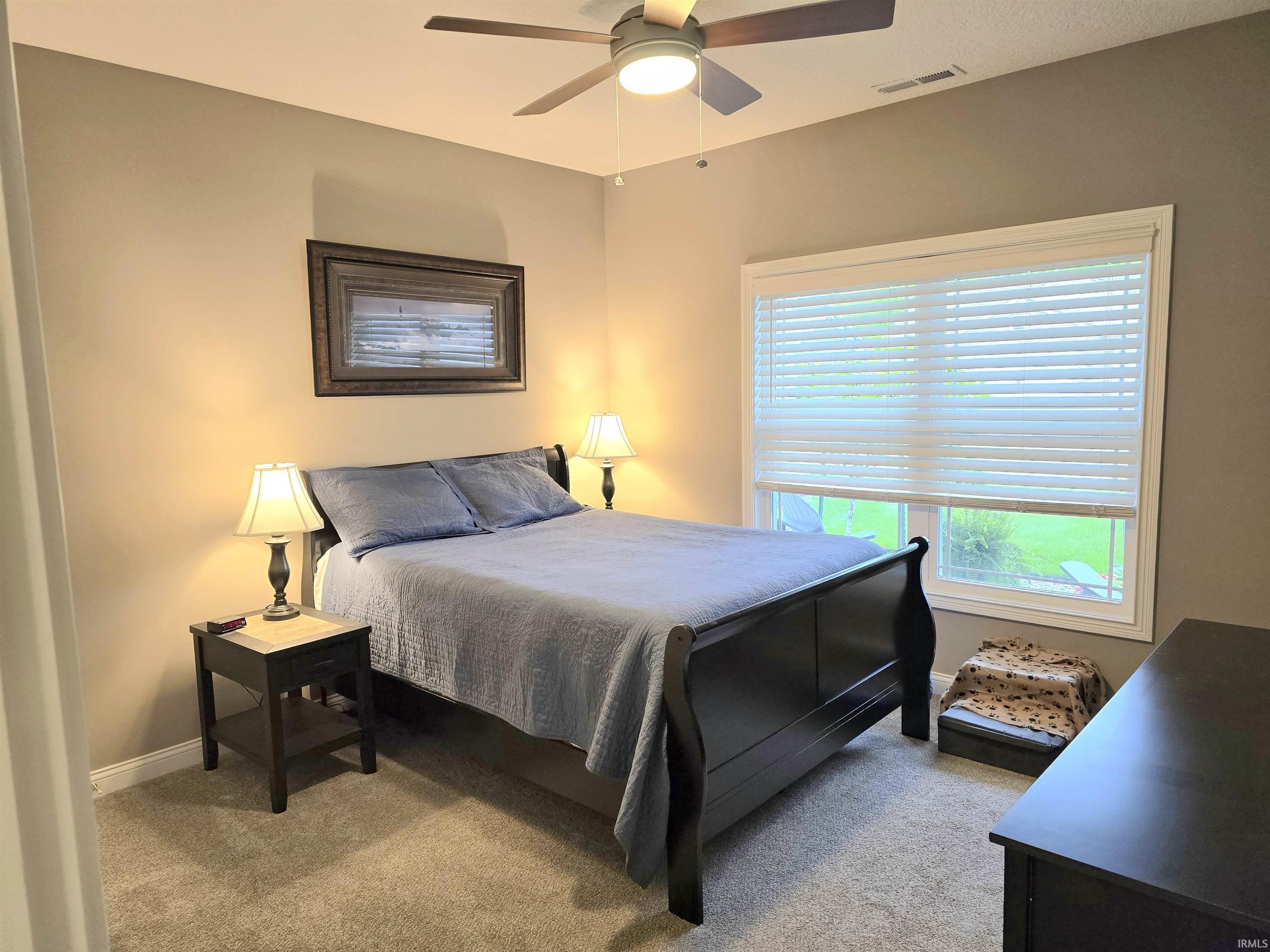 Carpeted room featuring a ceiling fan with integrated lighting, a large window with horizontal blinds, and neutral-toned walls