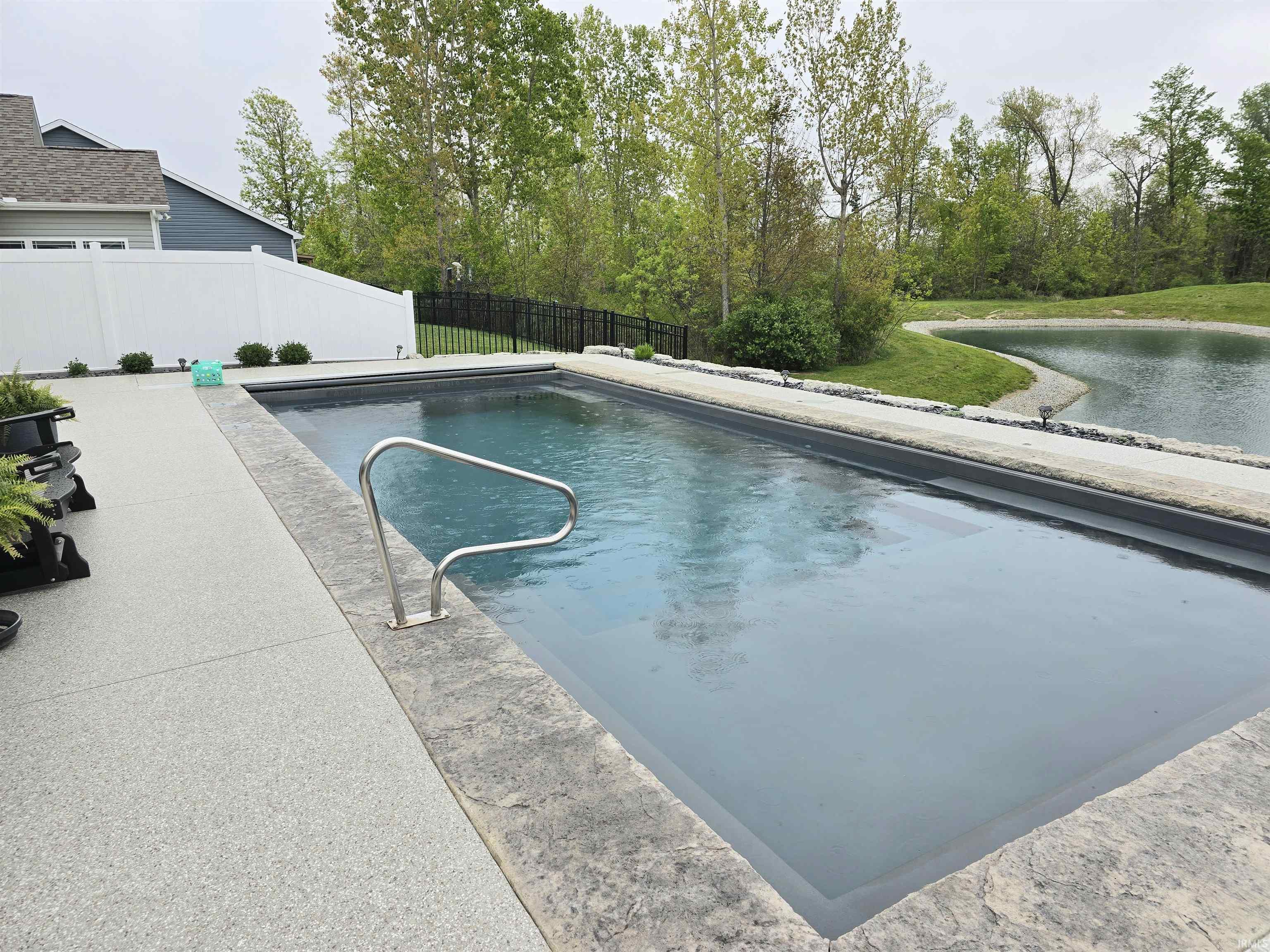 Rectangular inground pool with metal handrail and stamped concrete coping and electric pool cover.