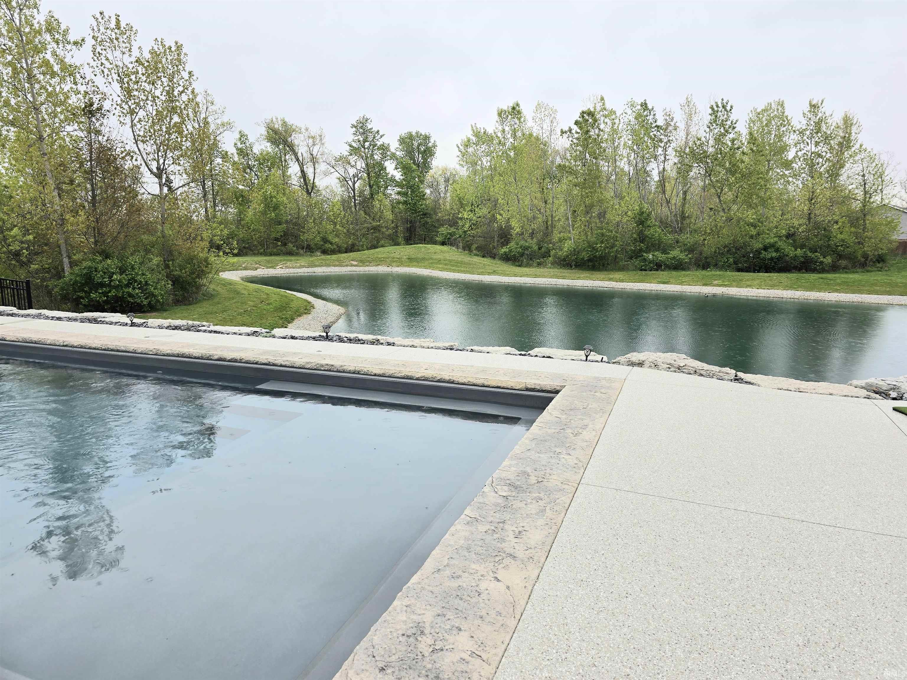 Outdoor swimming pool with a surrounding textured concrete patio, natural stone coping and amazing views of the pond.