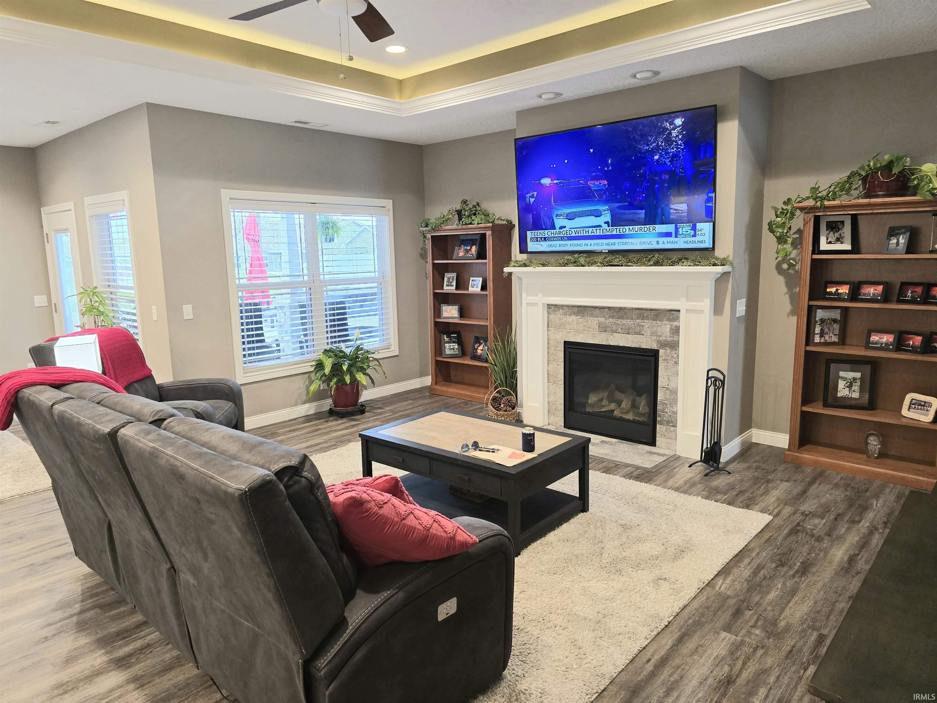 Living area showcasing a gas fireplace with a stone surround and white mantel, LVP flooring, a tray ceiling with recessed lighting, and a ceiling fan.