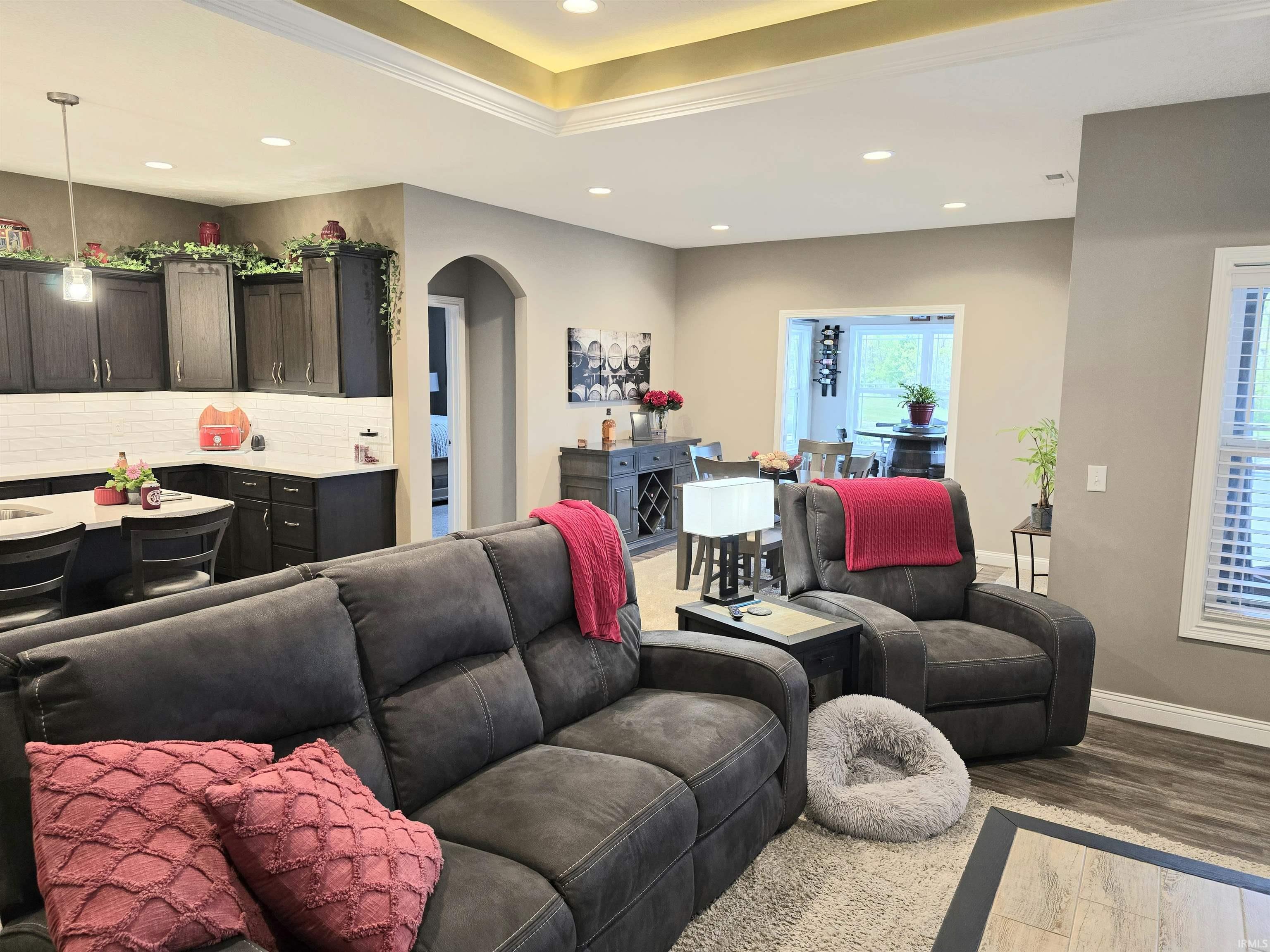 Open-concept living space featuring wood-finish flooring, a tray ceiling with recessed lighting, and an arched doorway