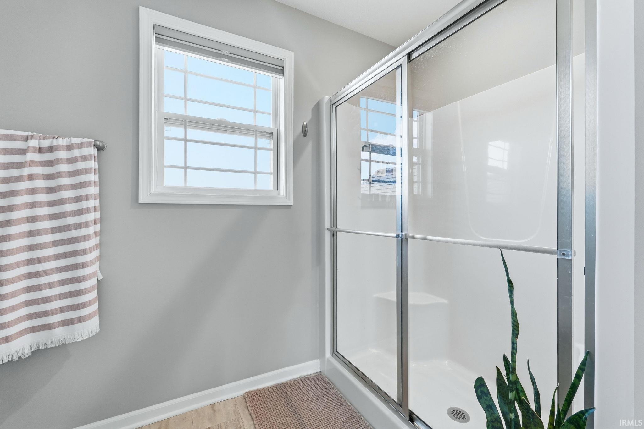 Bathroom featuring a glass-enclosed shower with a built-in bench, white shower surround, and a window with blinds