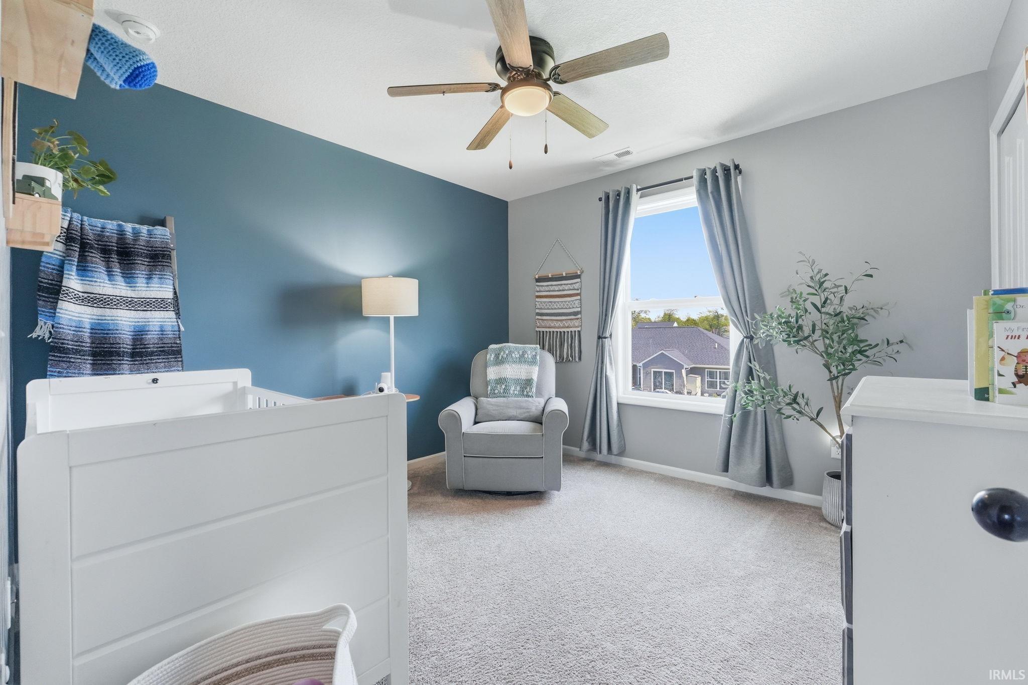 Carpeted room featuring a ceiling fan with integrated lighting, a single window with curtain rods, and a blue accent wall