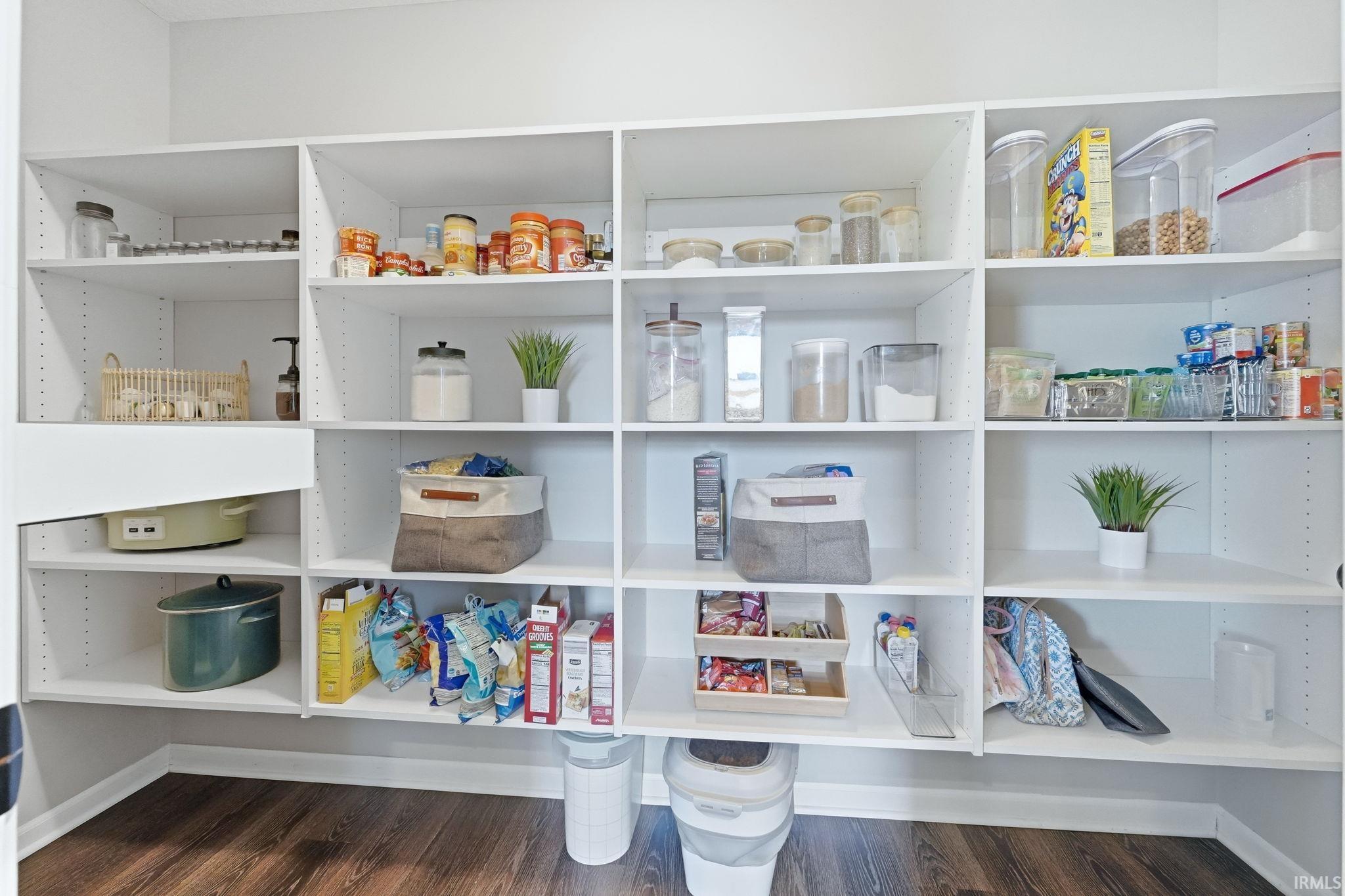 White built-in pantry shelving featuring extensive storage, adjustable shelf heights, a corner configuration, and wood-finish flooring