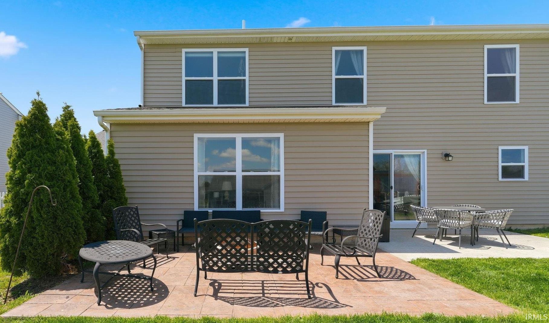 Expansive backyard featuring a stone paver patio, lush green lawn, mature evergreen privacy landscaping, and a sliding glass door for outdoor access