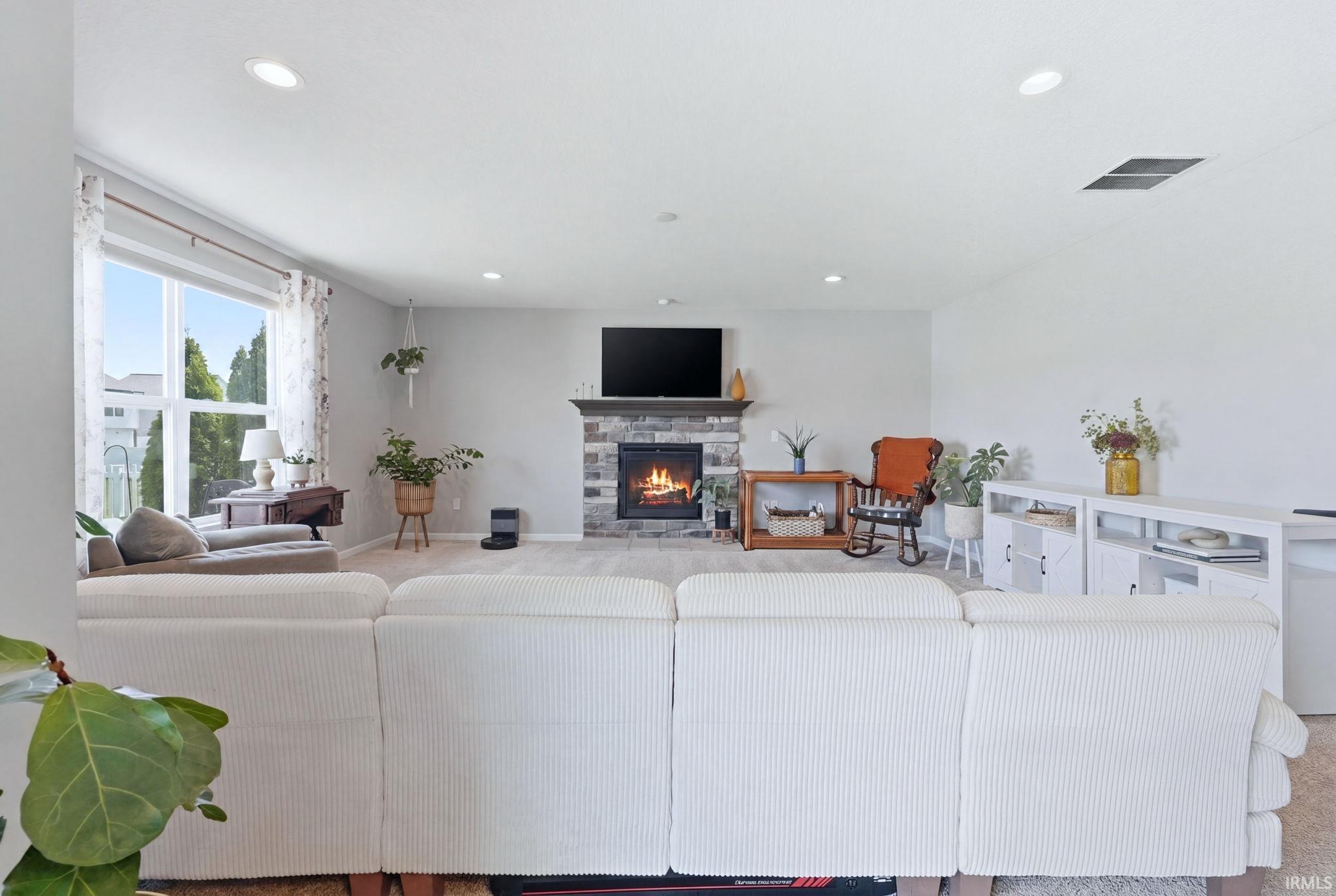 Spacious living area featuring a stone-clad fireplace with a wood mantel, large window with ample natural light, recessed ceiling lighting, and light-toned carpeting