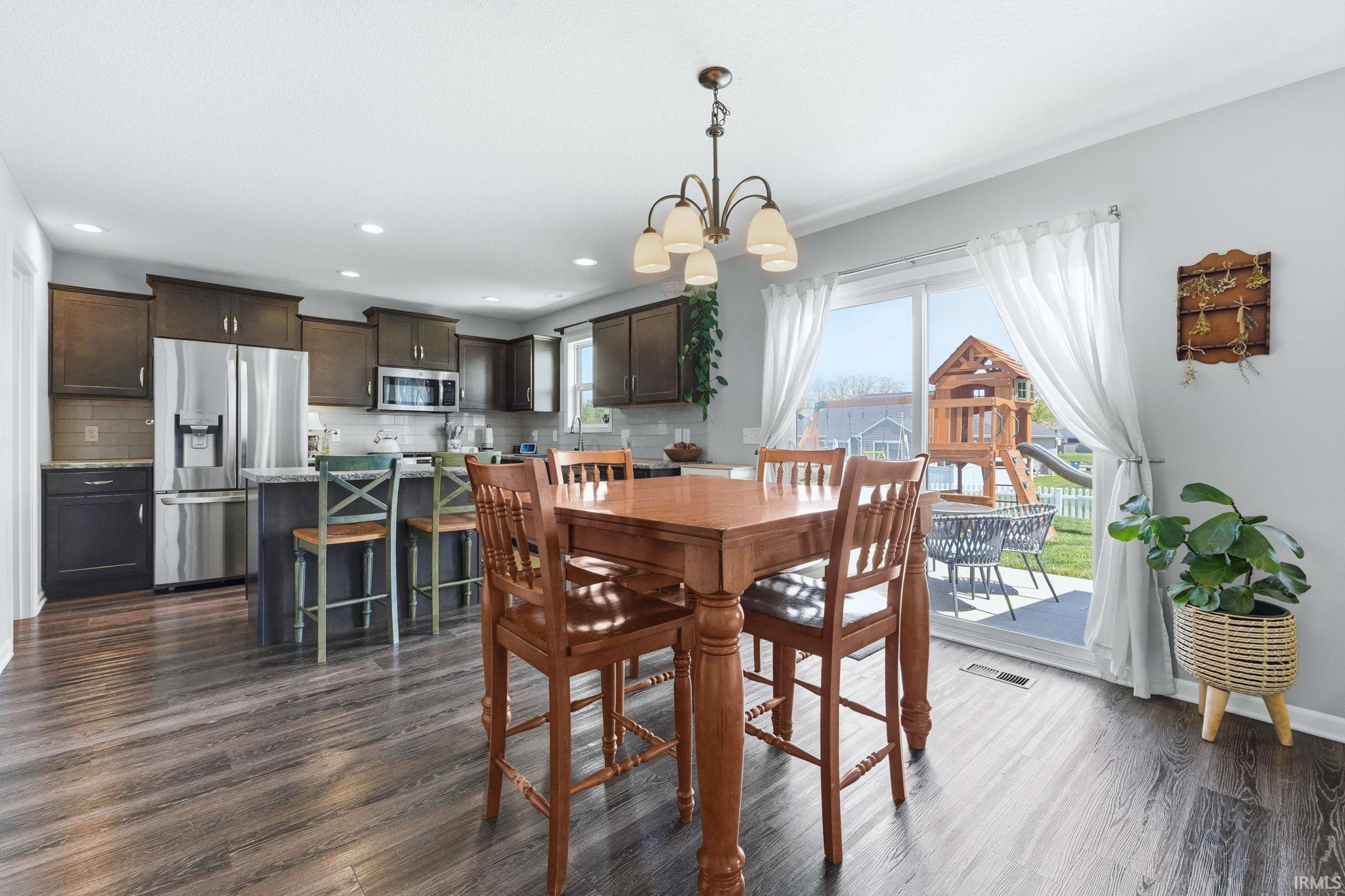 Kitchen and dining area featuring wood-finish flooring, dark wood cabinetry, stainless steel appliances, a center island with seating, and a sliding glass door to the exterior patio