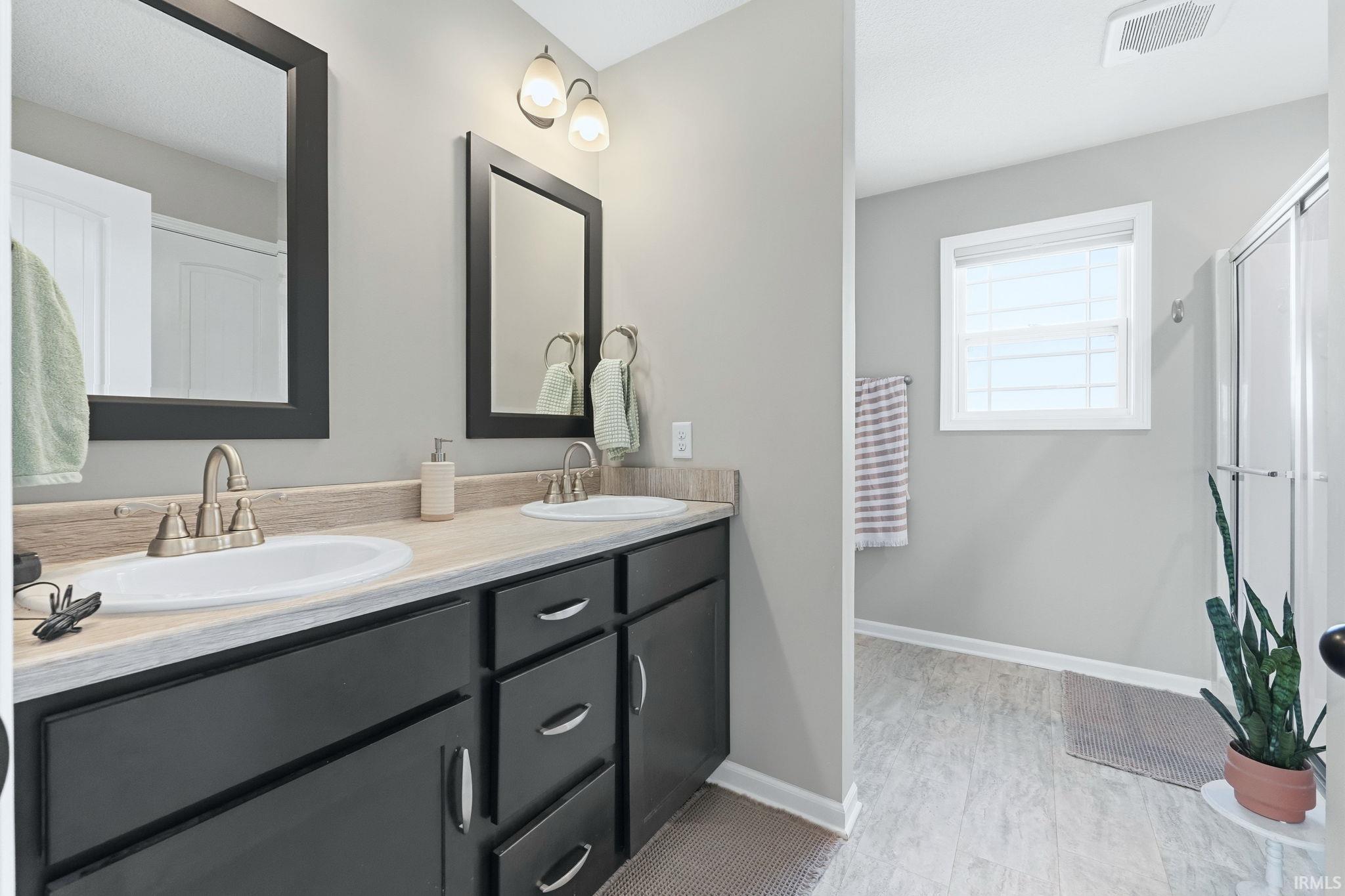 Bathroom featuring a dual vanity with dark cabinetry, dual mirrors, and brushed nickel fixtures
