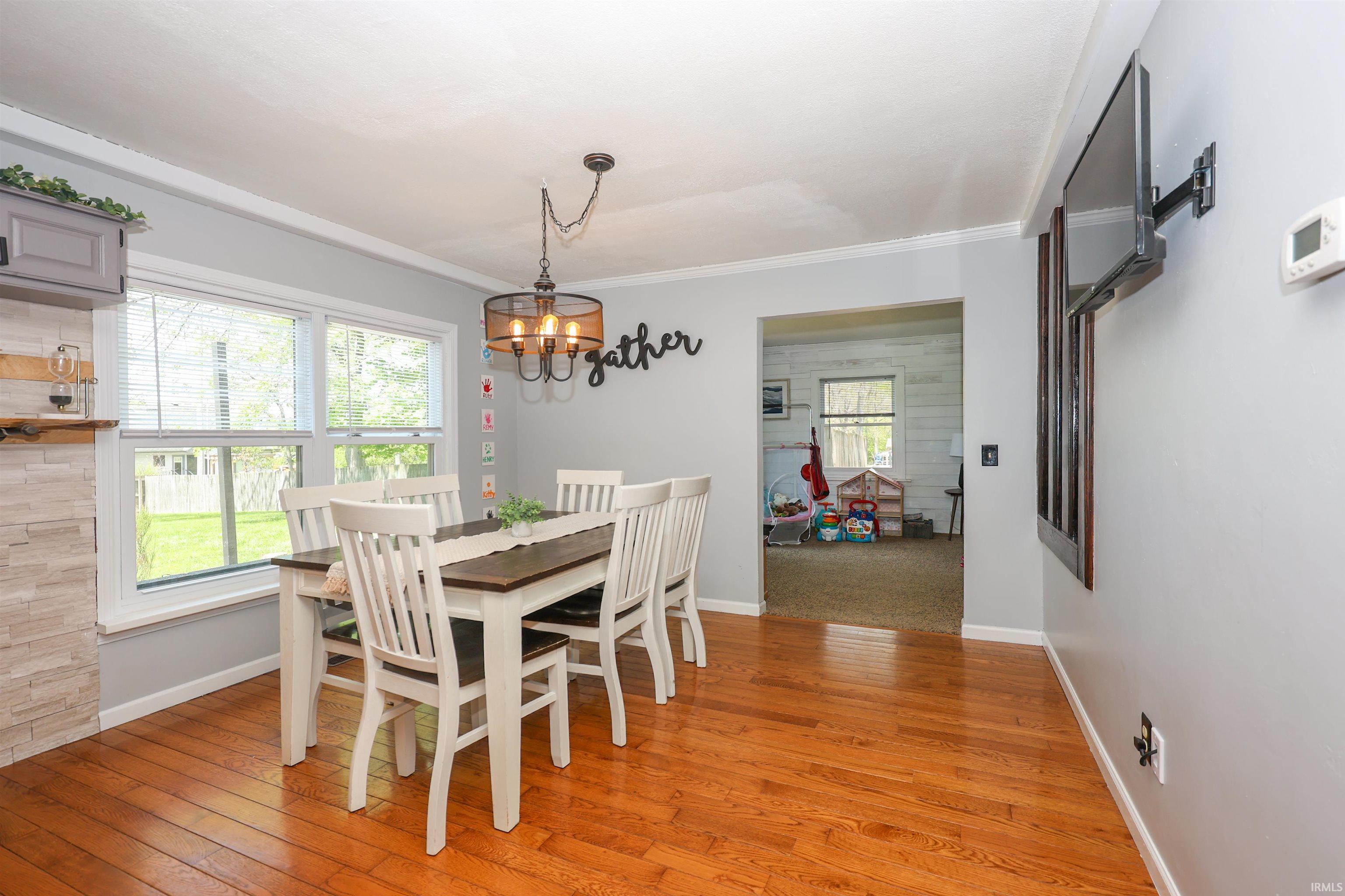 Bright dining area featuring wood-finish flooring, a contemporary chandelier, crown molding, and white trim