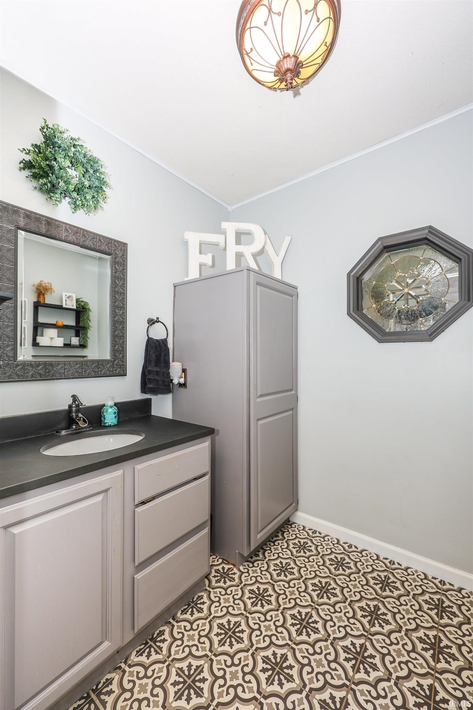 Bathroom featuring patterned floor tiling, single vanity with integrated sink and dark countertop, and coordinating tall cabinetry