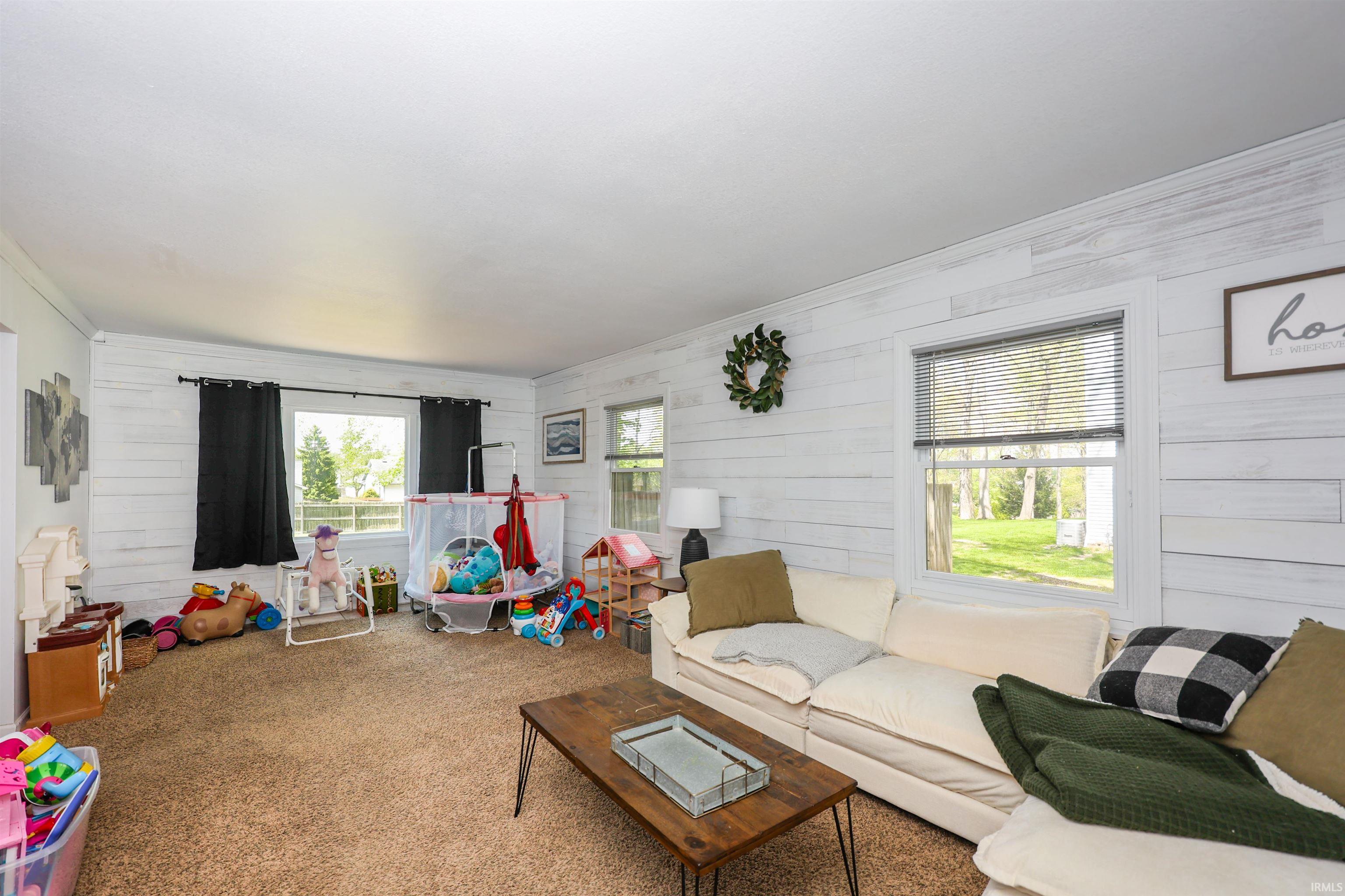 Spacious room featuring light-toned shiplap walls, multiple windows providing natural light, and neutral-toned carpeting