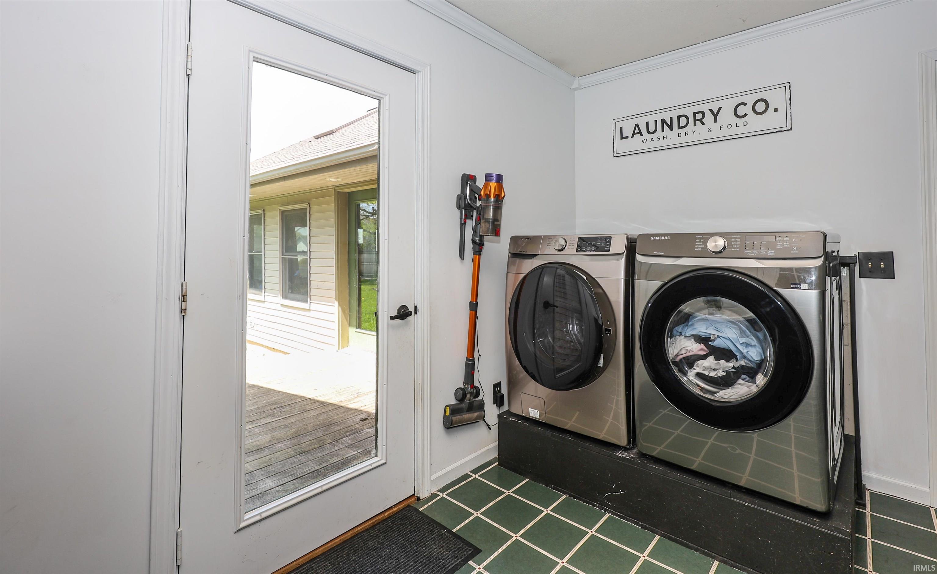 Laundry area featuring a full-light exterior door, green square tile flooring, white painted walls, and an exterior wood deck