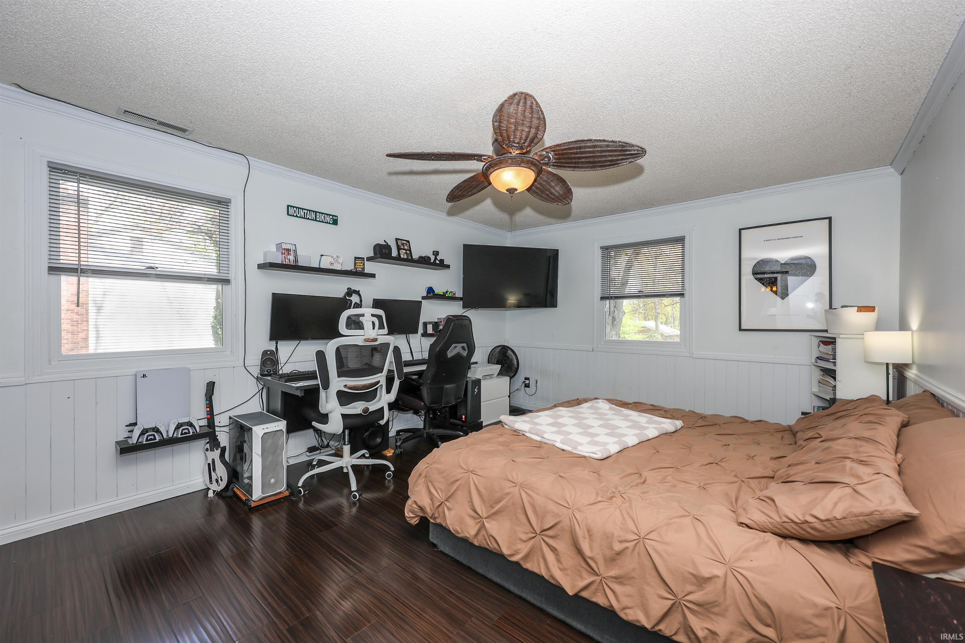 Spacious room featuring dark wood-finish flooring, white paneled wainscoting, and a textured ceiling