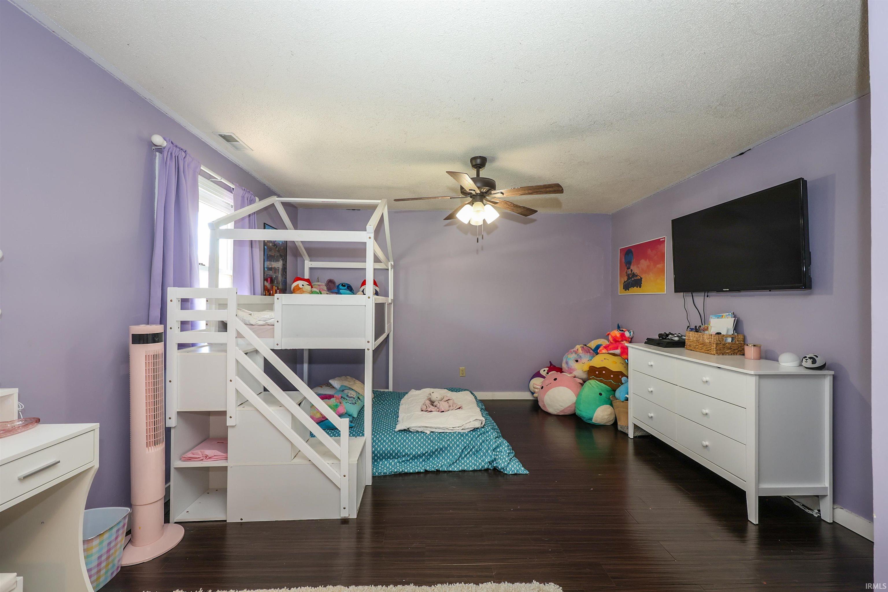 Room featuring dark wood-finish flooring, a ceiling fan with integrated lighting, and a window with light-colored curtains