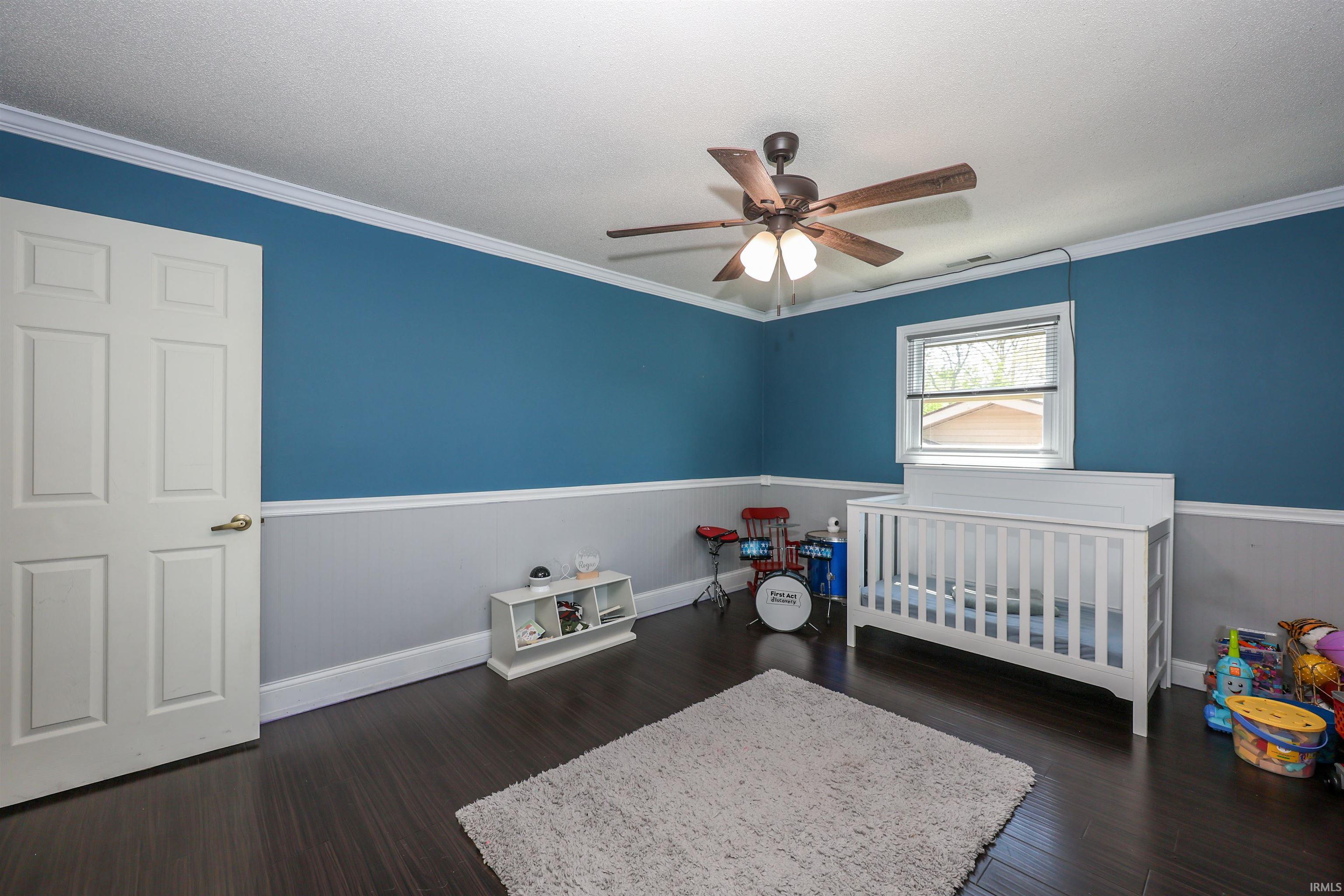 Bedroom featuring dark wood-finish flooring, two-tone wall treatment with a blue upper and light gray lower, white crown molding, and a ceiling fan with light fixture