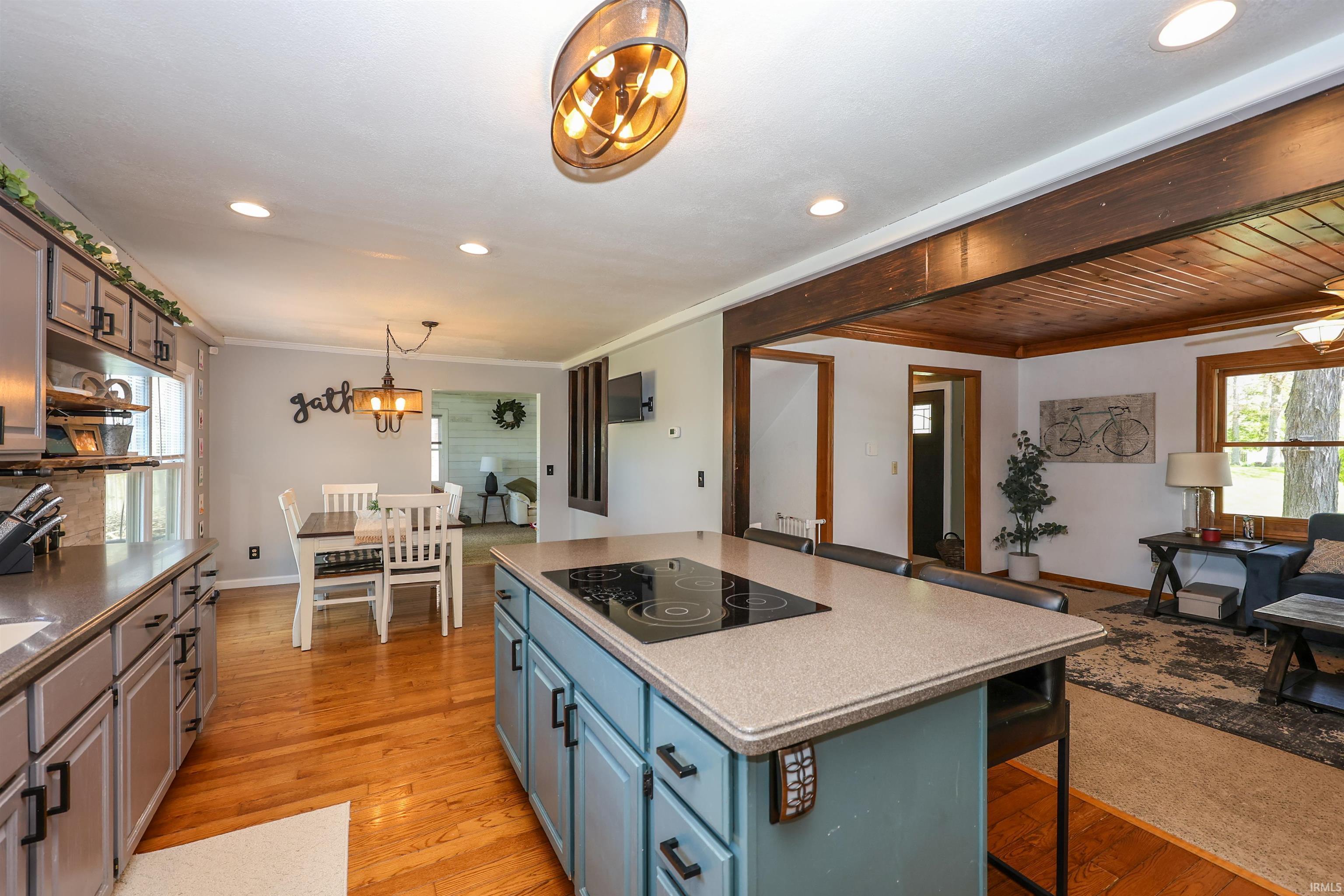 Kitchen featuring wood-finish flooring, a central island with an integrated cooktop, painted cabinetry, recessed lighting, and a dining area with a chandelier