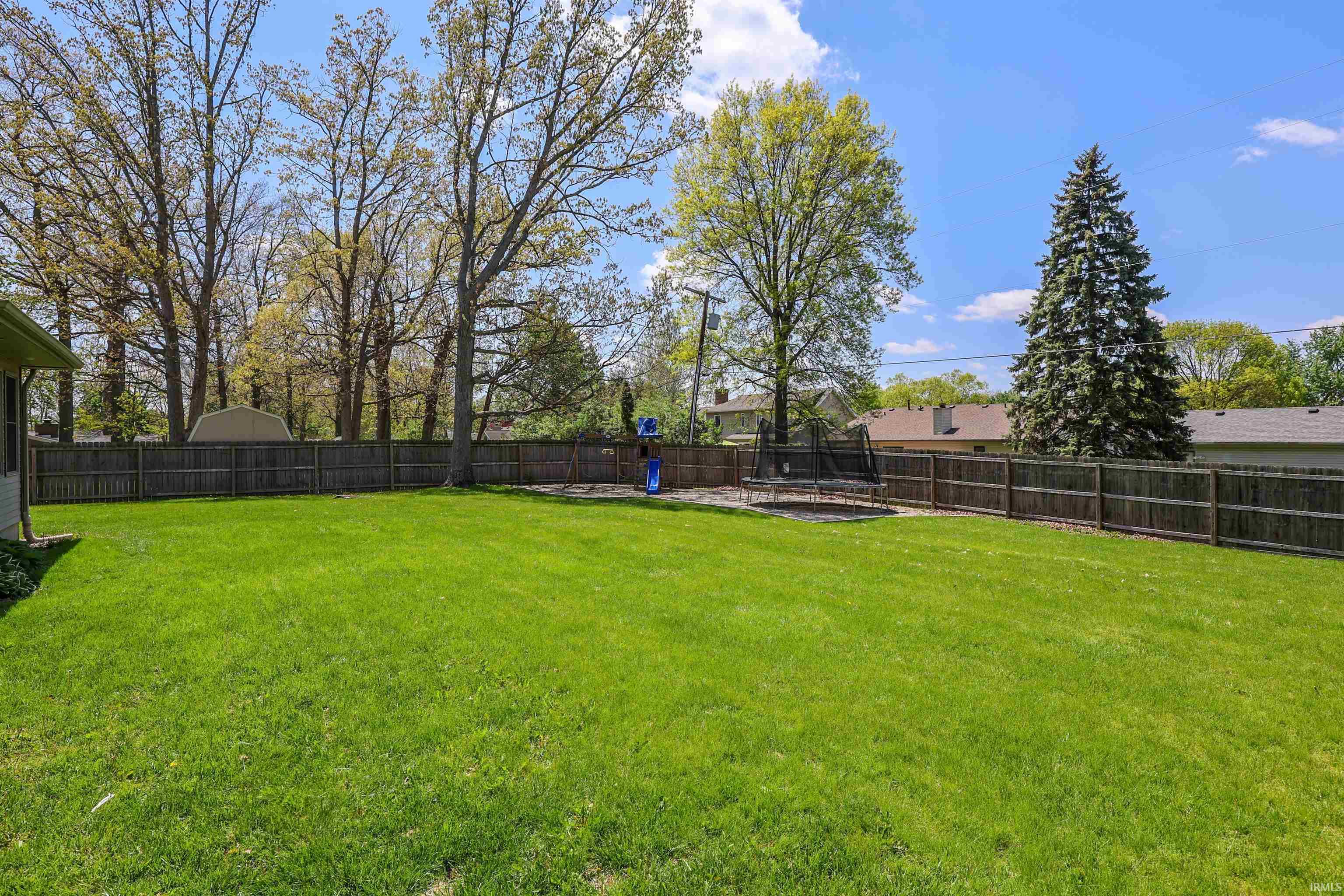 Expansive backyard with a manicured lawn, full perimeter wood fencing, and mature trees providing natural screening