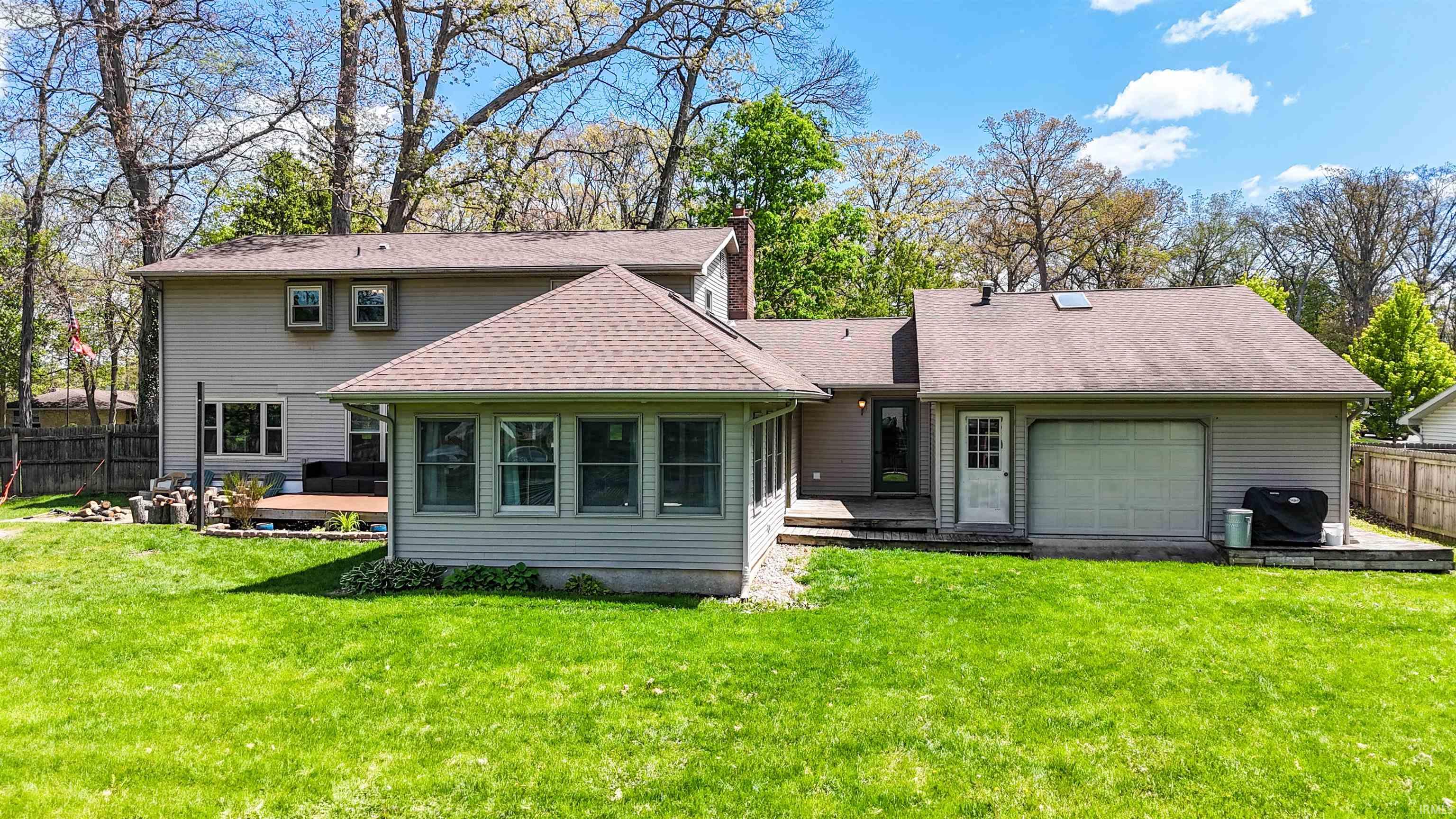 Rear exterior featuring a sunroom, a multi-level wood deck, an attached garage with a white overhead door, and a light gray siding finish
