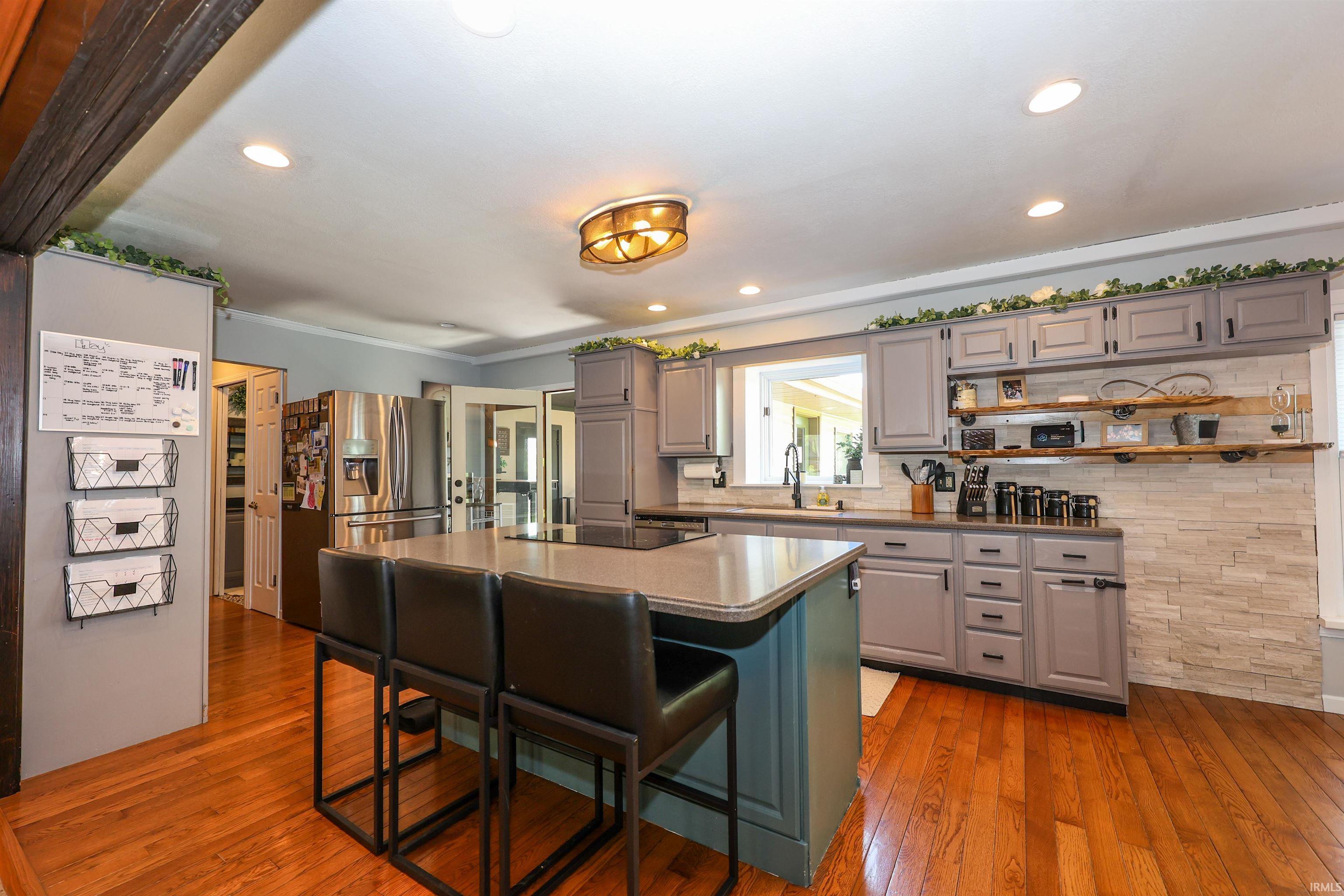 Spacious kitchen featuring hardwood flooring, a central island with seating, gray cabinetry, stainless steel appliances, and a stacked stone backsplash