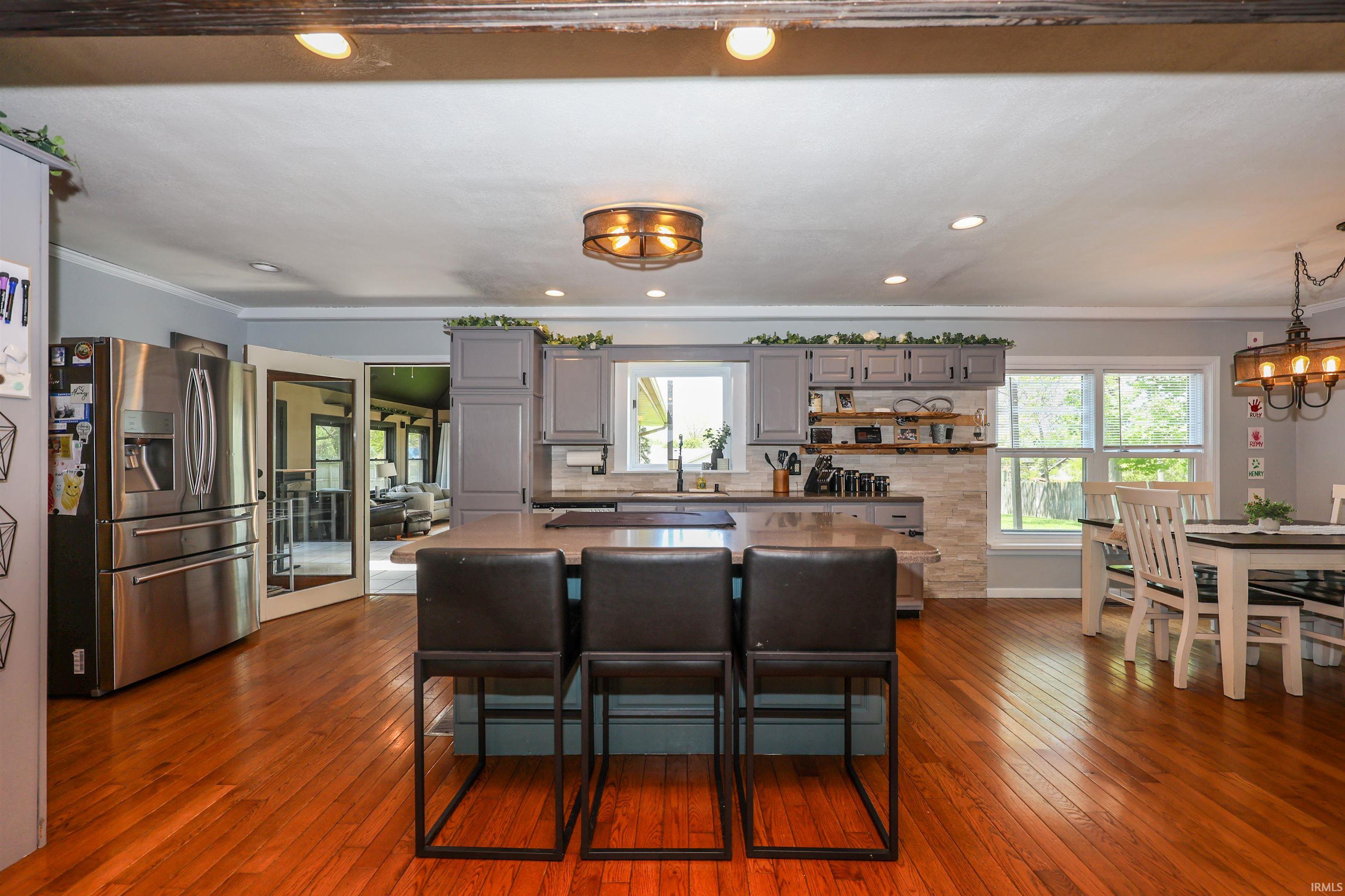 Spacious kitchen featuring wood-finish flooring, a central island with seating, grey cabinetry, stainless steel appliances, and a dining area with a chandelier