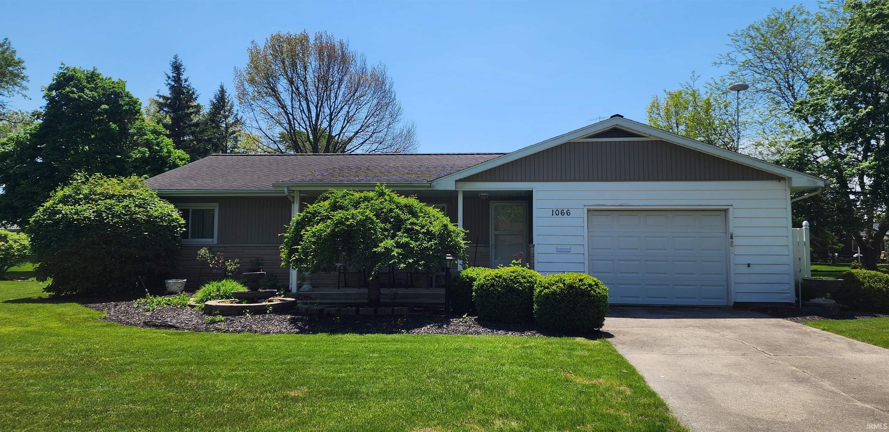 Ranch-style residence featuring a single-car garage, mature landscaping, a paved driveway, and a well-kept lawn