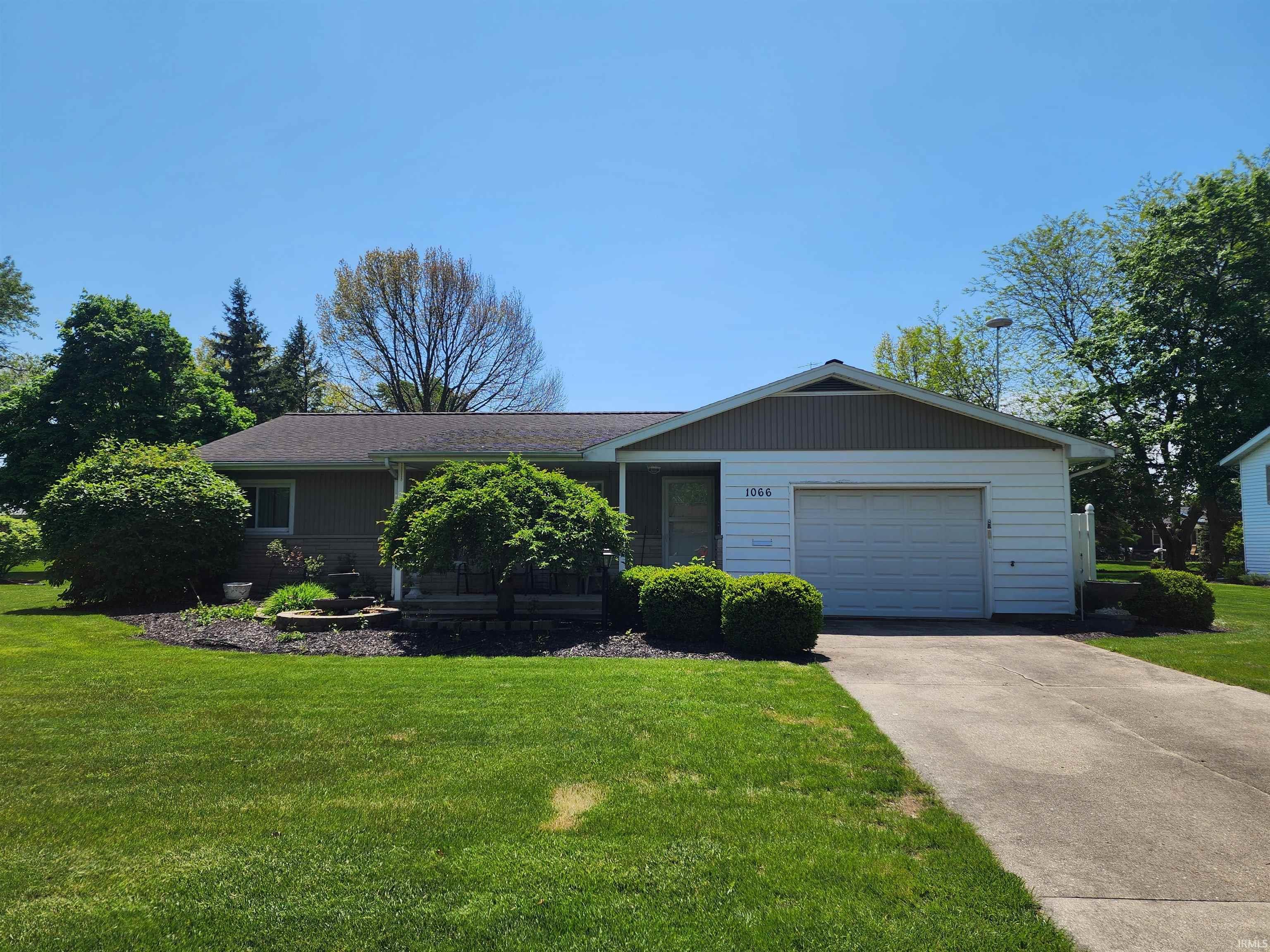 Ranch-style residence featuring a single-car garage with white door, light brown siding, and a dark shingle roof