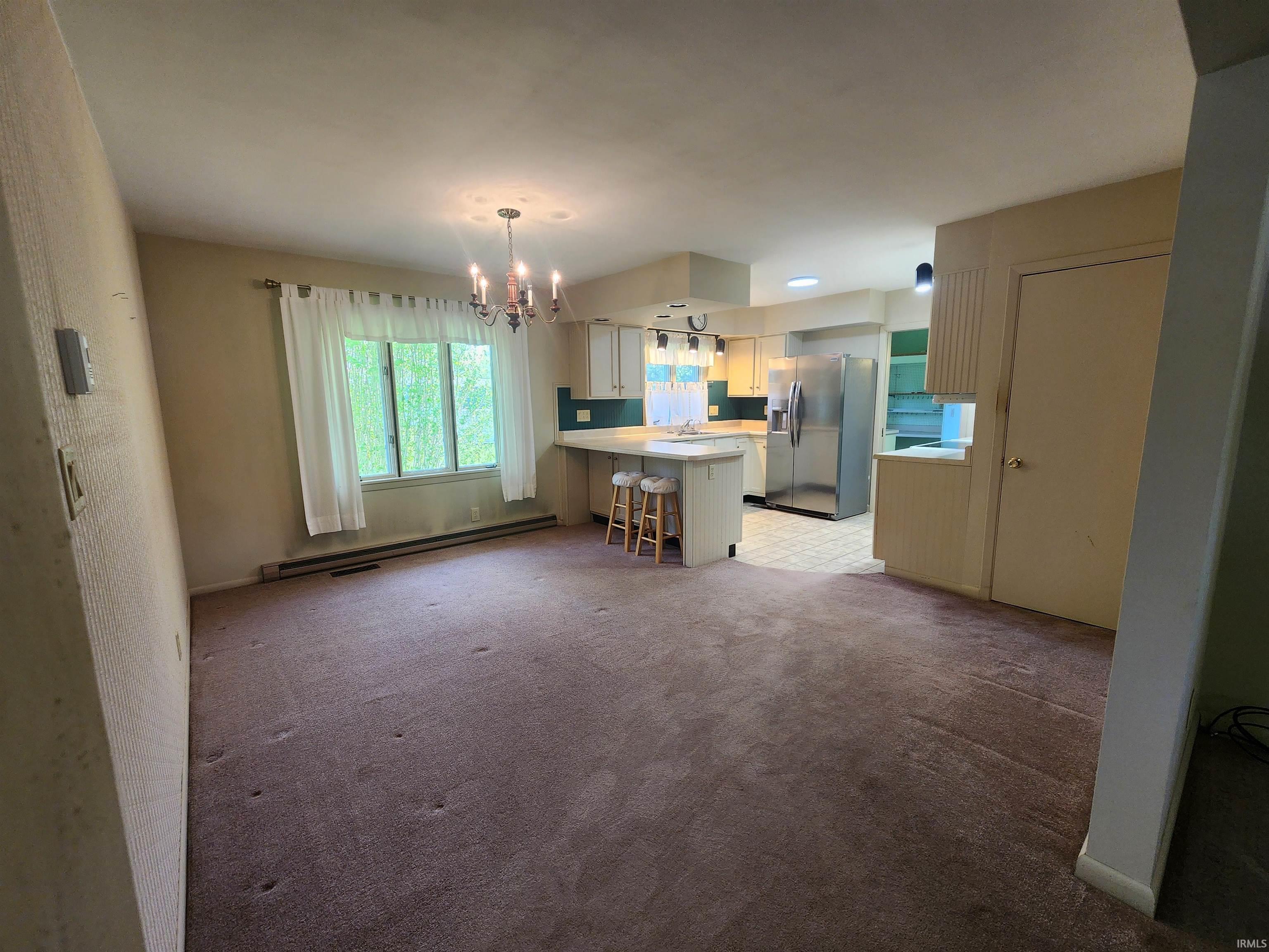 Open-concept living space featuring a carpeted floor, large window with natural light, and a prominent chandelier
