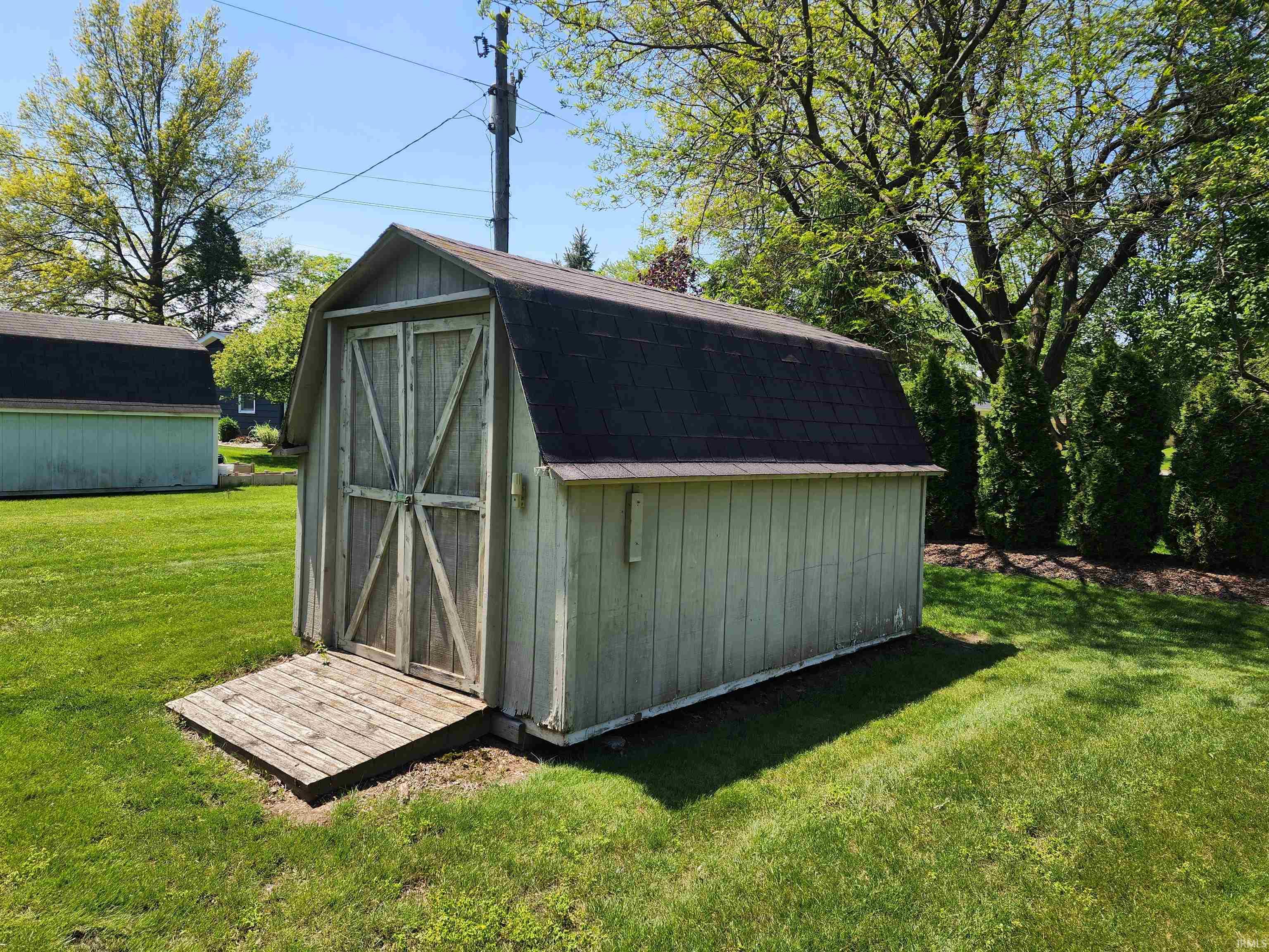 Freestanding storage shed with gambrel roof and double barn doors, set on a manicured lawn