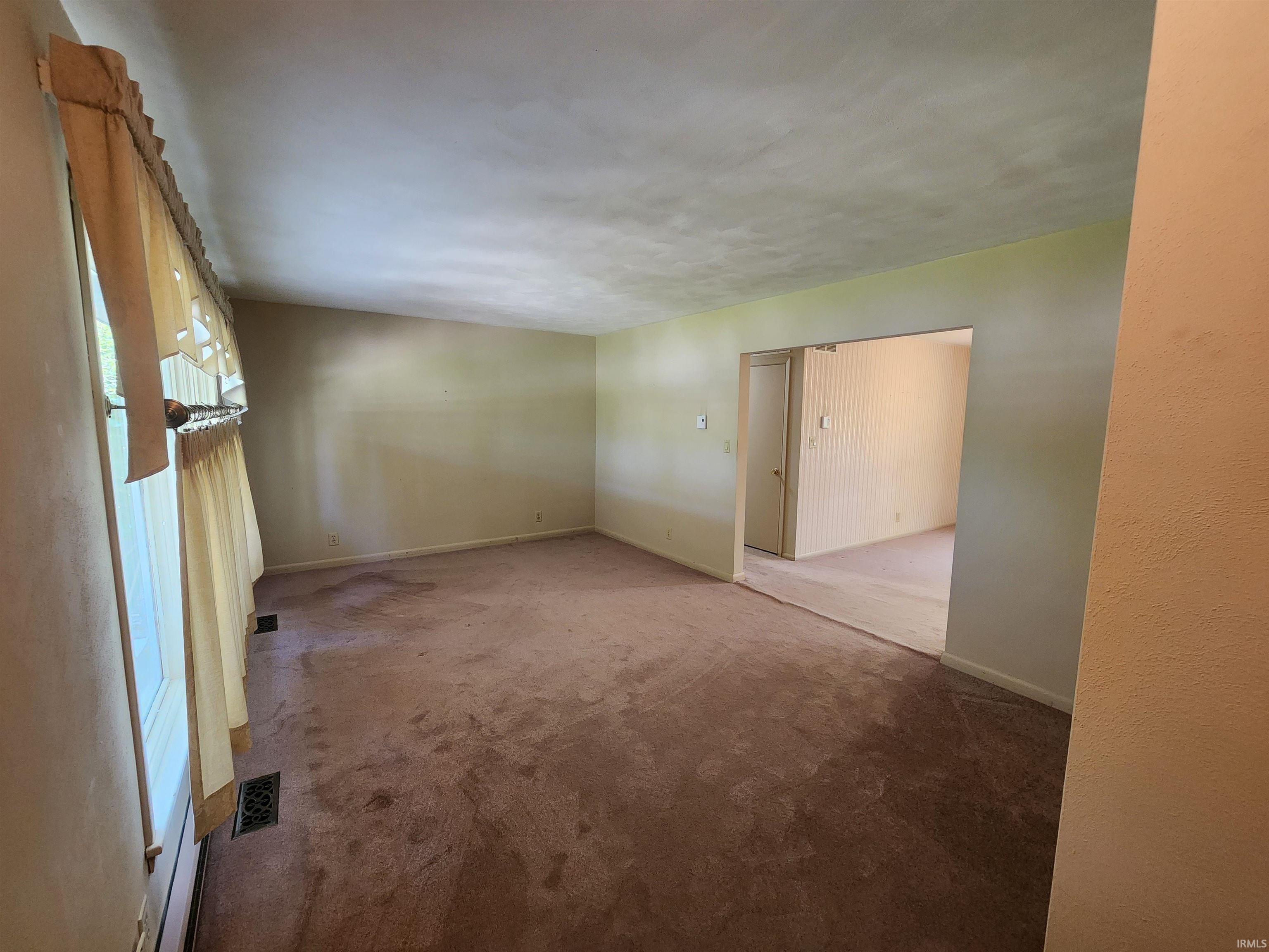 Spacious room featuring neutral wall tones and a window with a valance and curtains