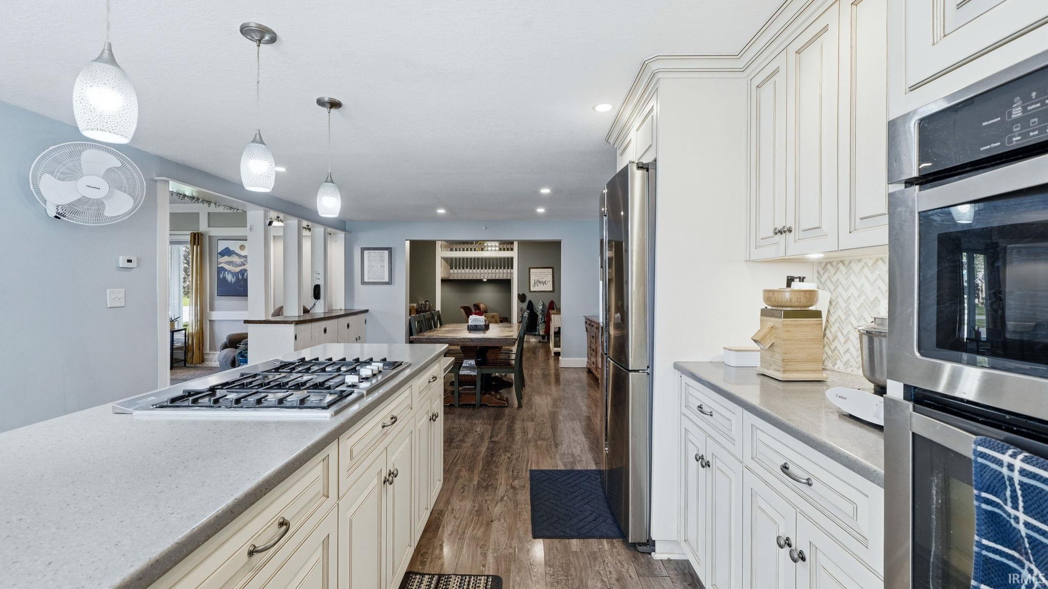 Kitchen featuring an island with a built-in gas cooktop, quartz countertops, white cabinetry, stainless steel appliances, and wood-finish flooring