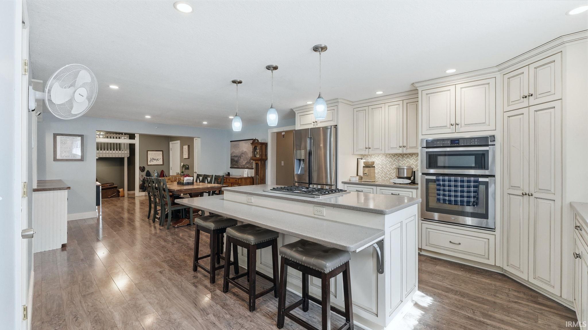 Expansive kitchen featuring a central island with a gas cooktop, light-toned cabinetry, stainless steel double ovens, and wood-finish flooring