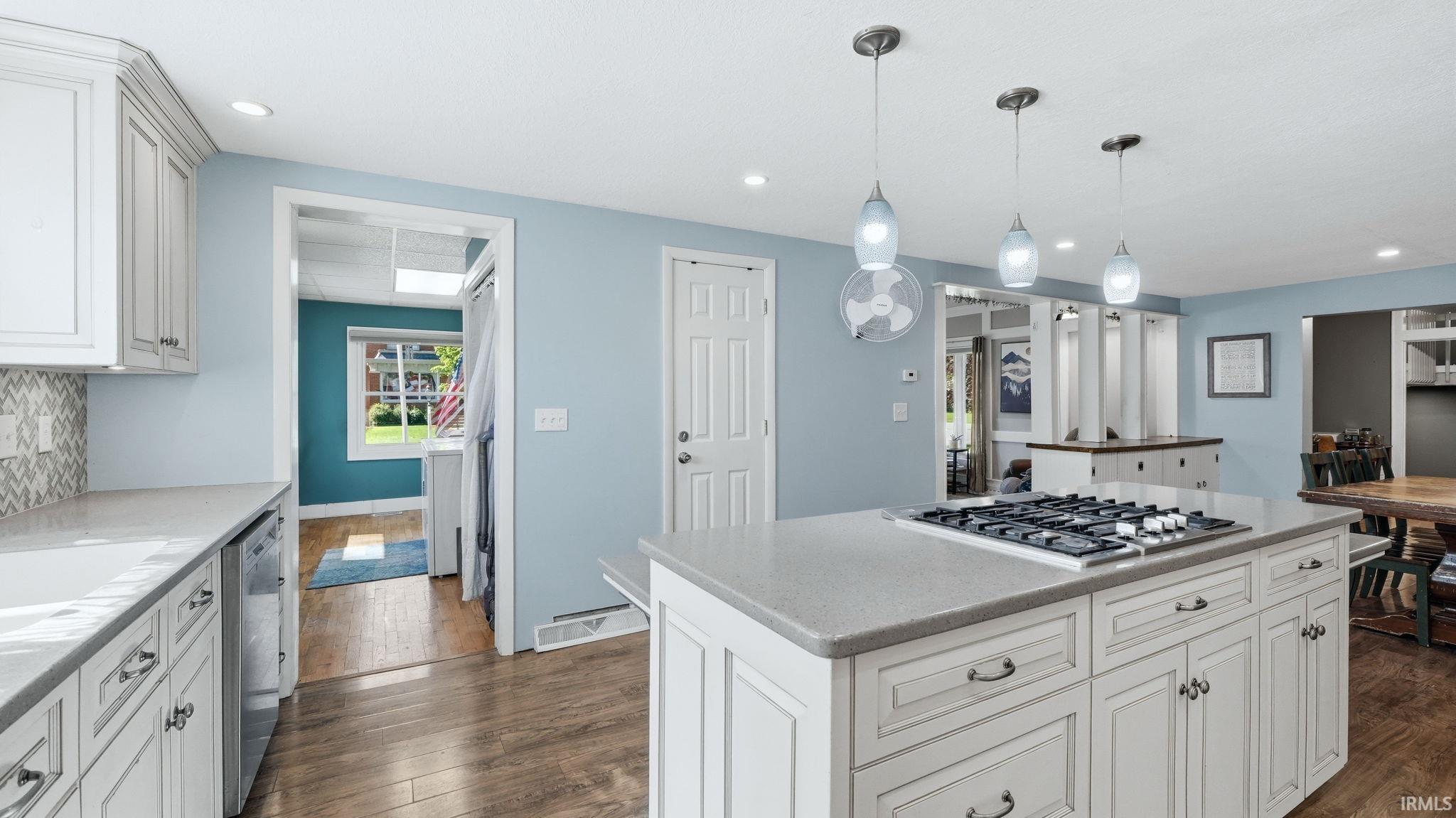 Kitchen featuring a central island with a built-in cooktop, light-toned cabinetry, light-colored countertops, a tile backsplash, and wood-finish flooring