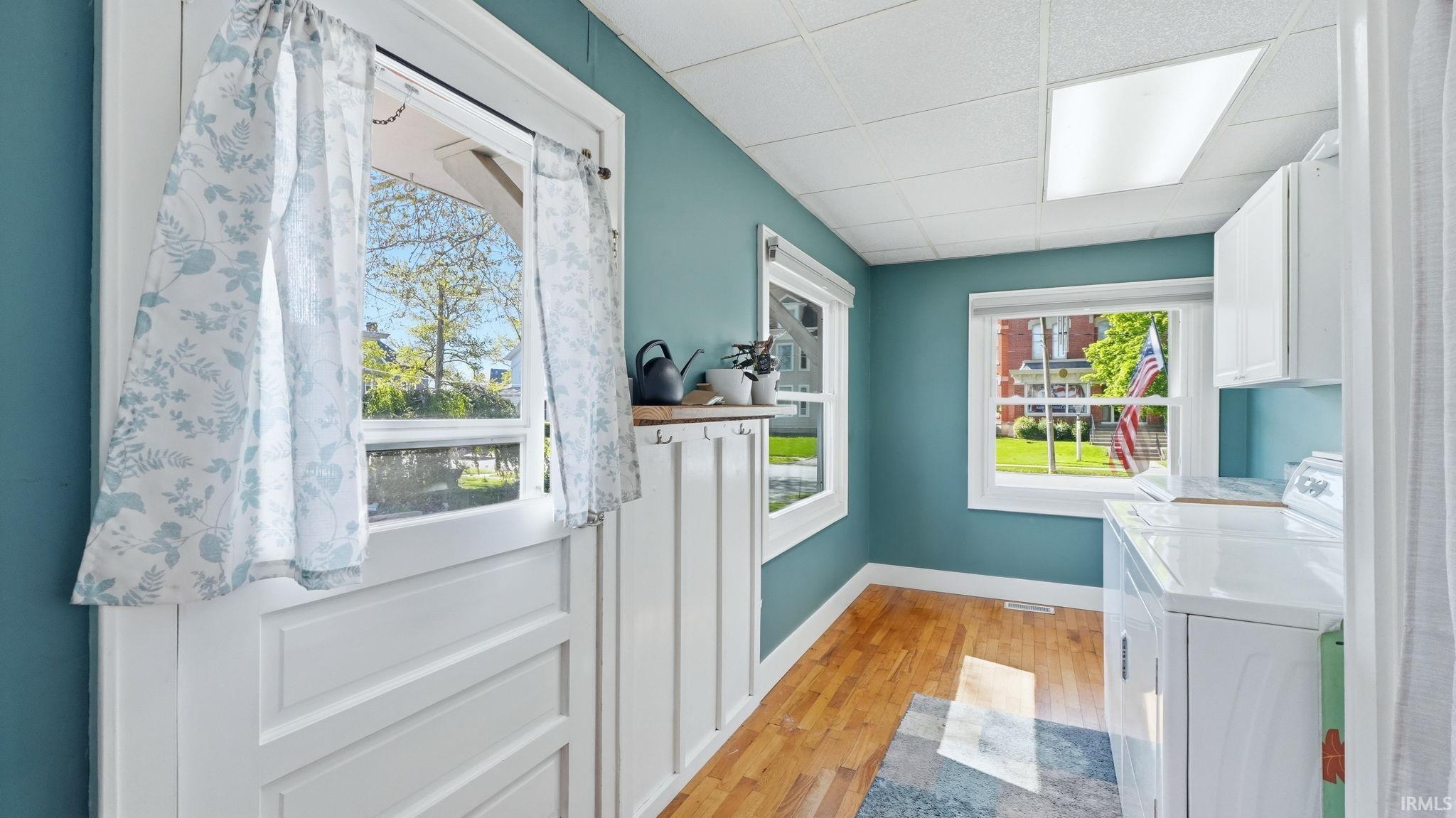 Laundry room featuring wood-finish flooring, white cabinetry, a built-in countertop, and white framed windows