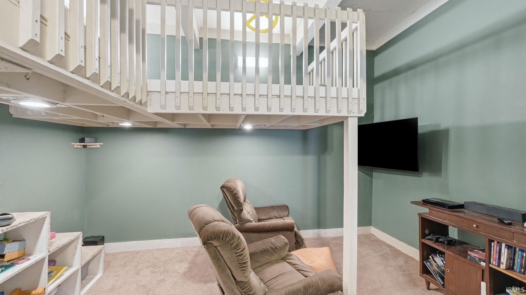 Carpeted recreation room featuring a built-in elevated loft with white wood railing, recessed lighting, and pale green walls