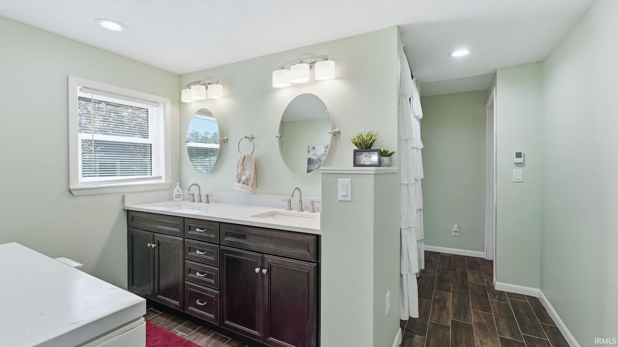 Bathroom featuring a dual vanity with dark wood-finish cabinetry, white countertops, and two oval mirrors