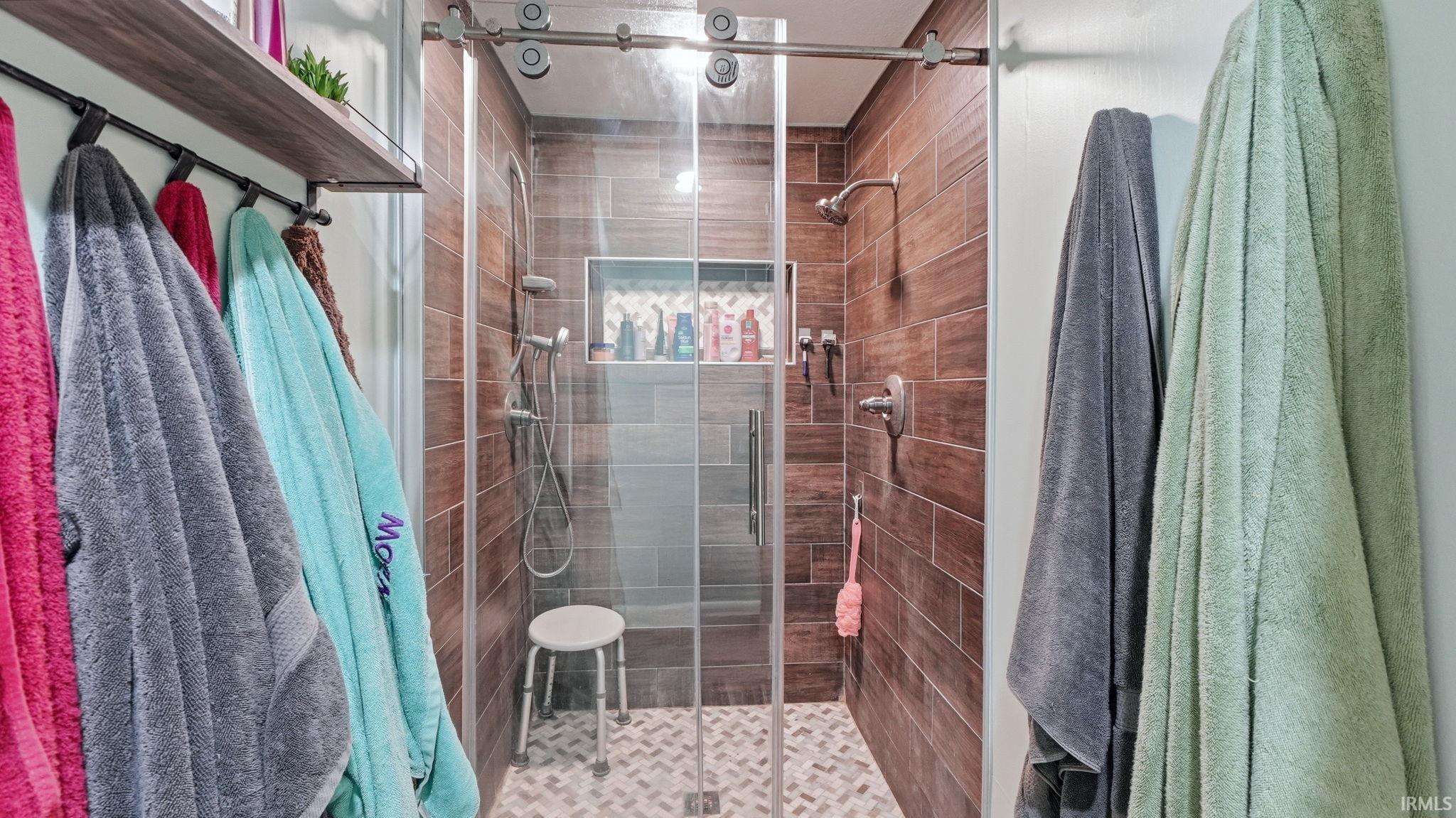 Walk-in shower featuring wood-finish tile walls, a mosaic-tiled floor, and a built-in shower niche