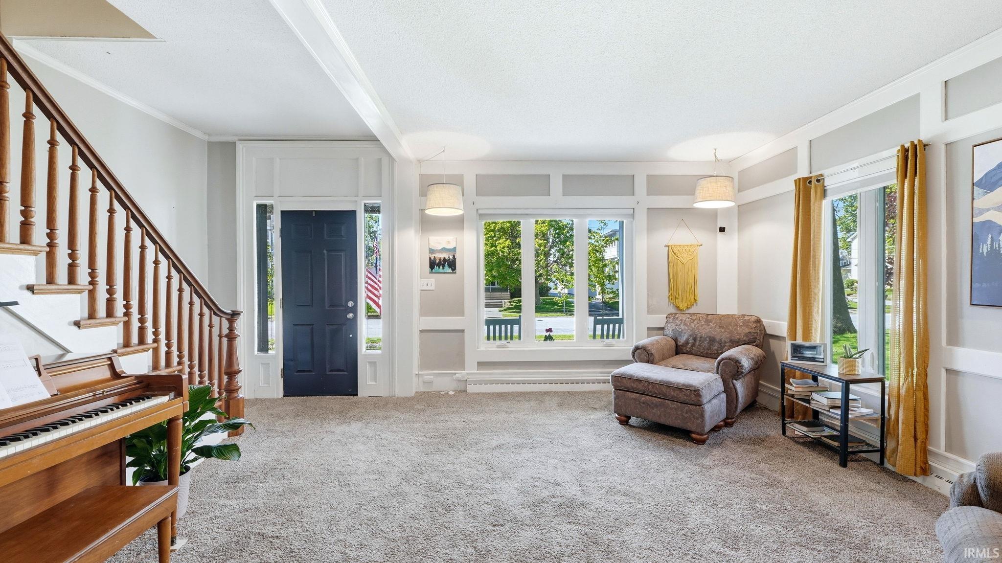 Spacious living area featuring light gray carpeting, a prominent wood staircase with white risers, and a dark paneled front door with sidelights