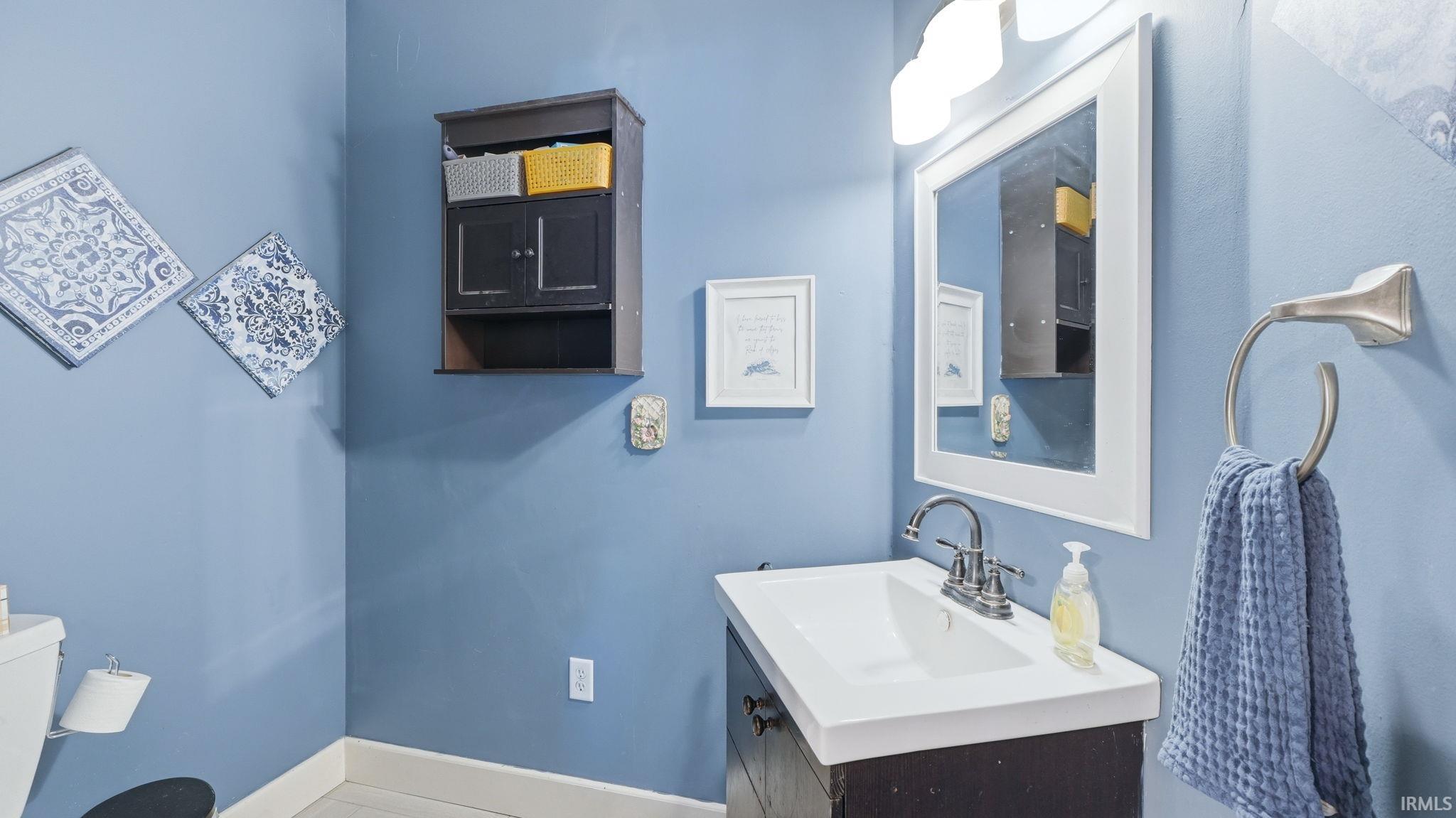 Bathroom featuring a single vanity with integrated sink, chrome faucet, wall-mounted mirror, and overhead light fixture