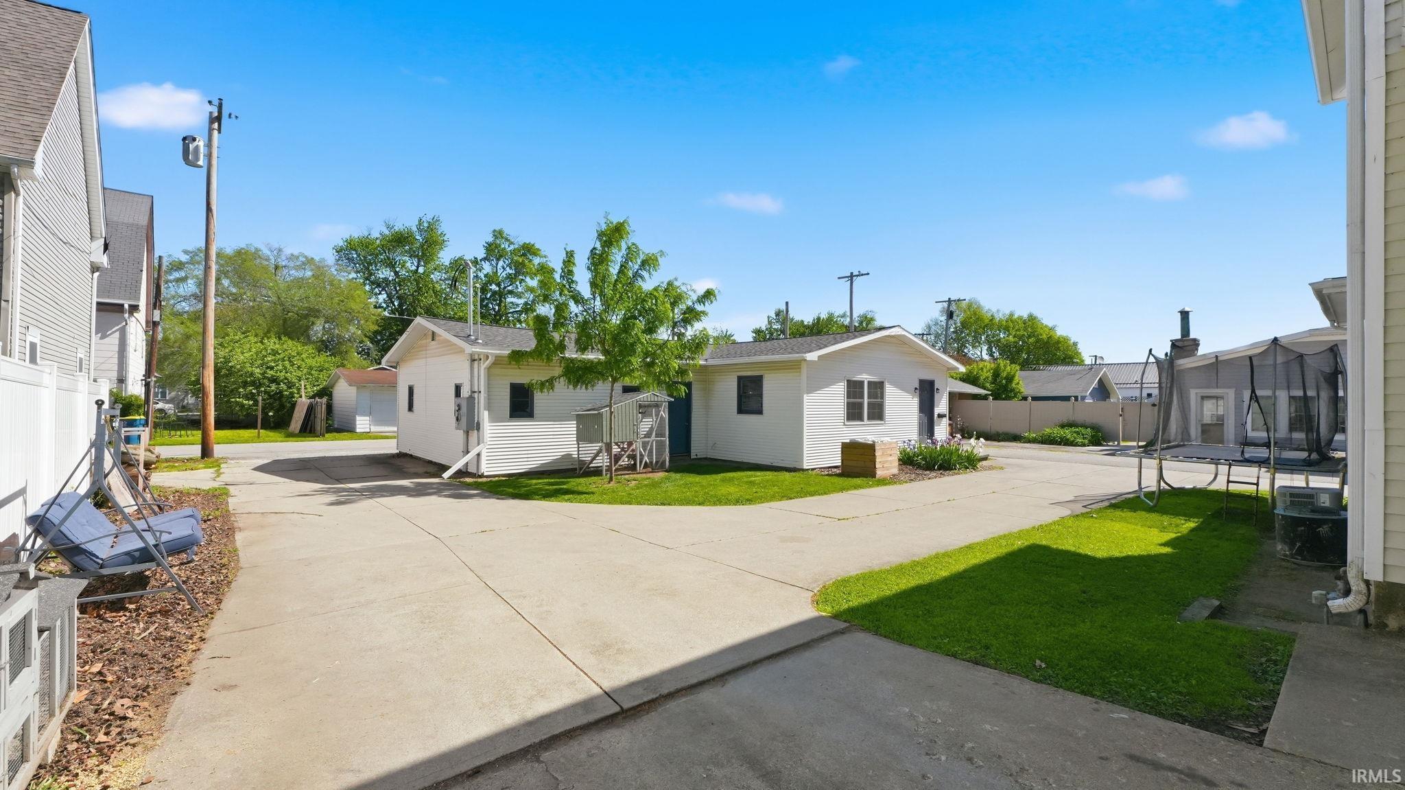 Expansive concrete driveway providing access to two detached structures and a fenced yard with established landscaping
