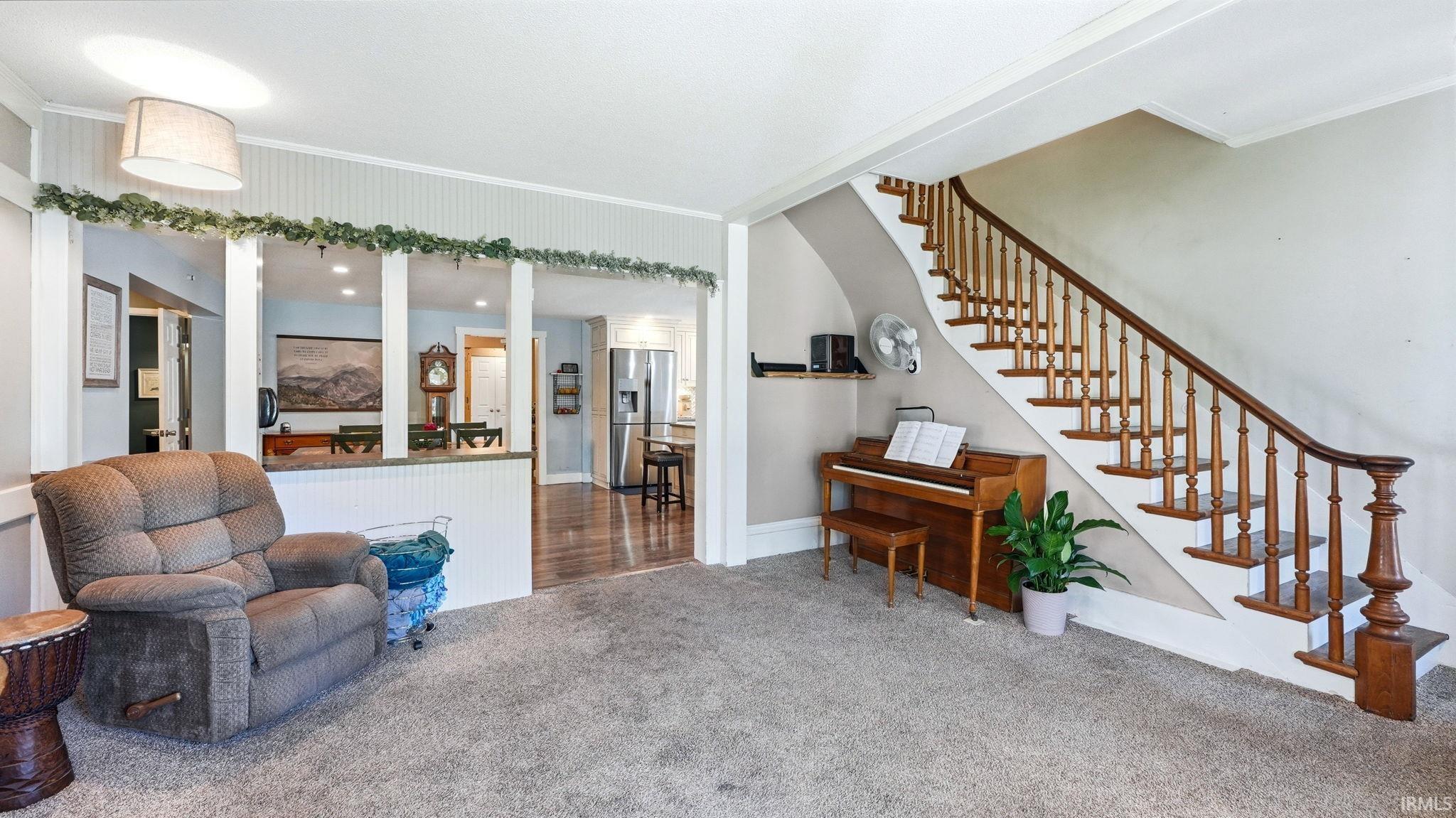 Carpeted living area featuring a wood staircase with traditional balusters, a half-wall with beadboard paneling, and an overhead light fixture