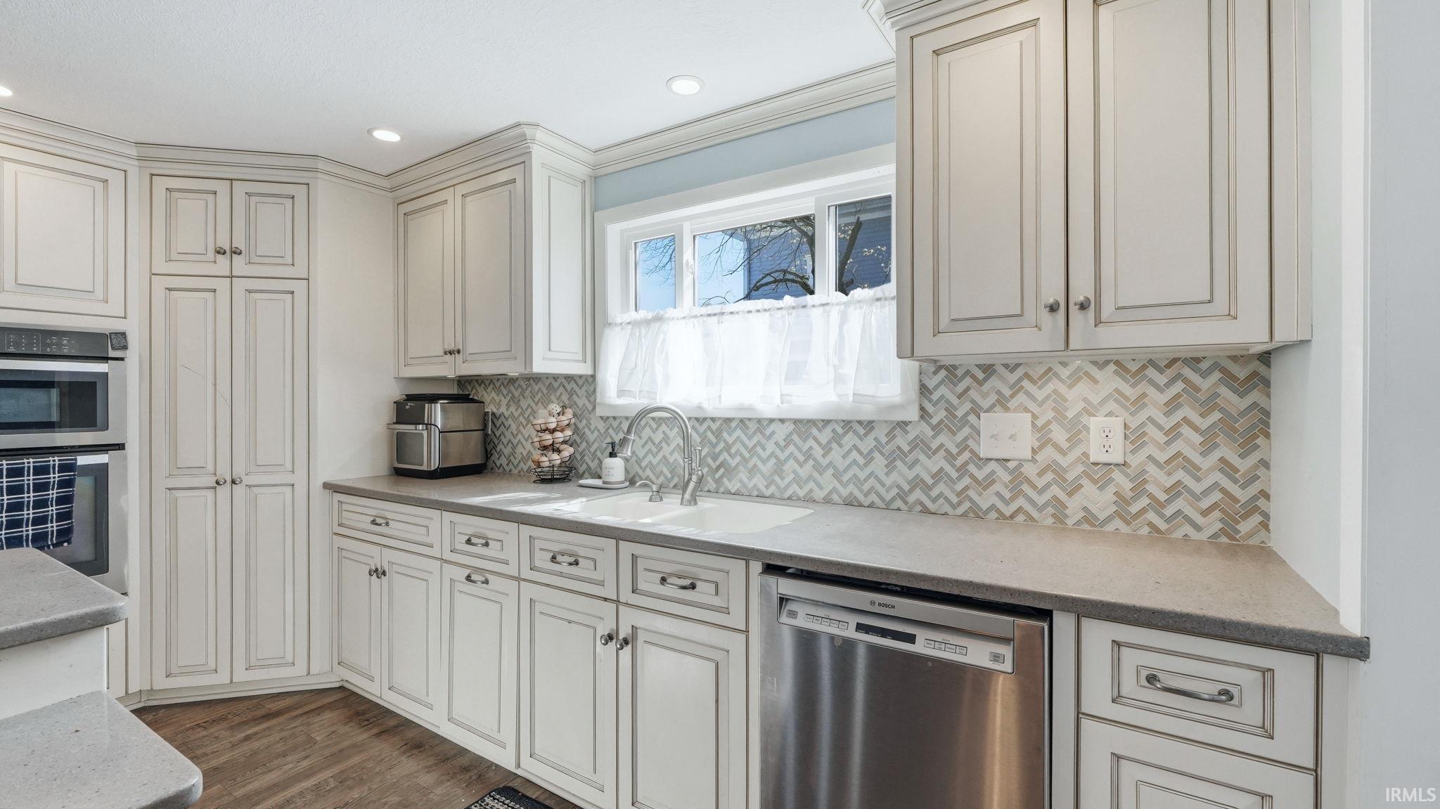 Kitchen featuring white cabinetry with dark hardware, a herringbone pattern backsplash, a stainless steel dishwasher, a built-in oven, and recessed lighting