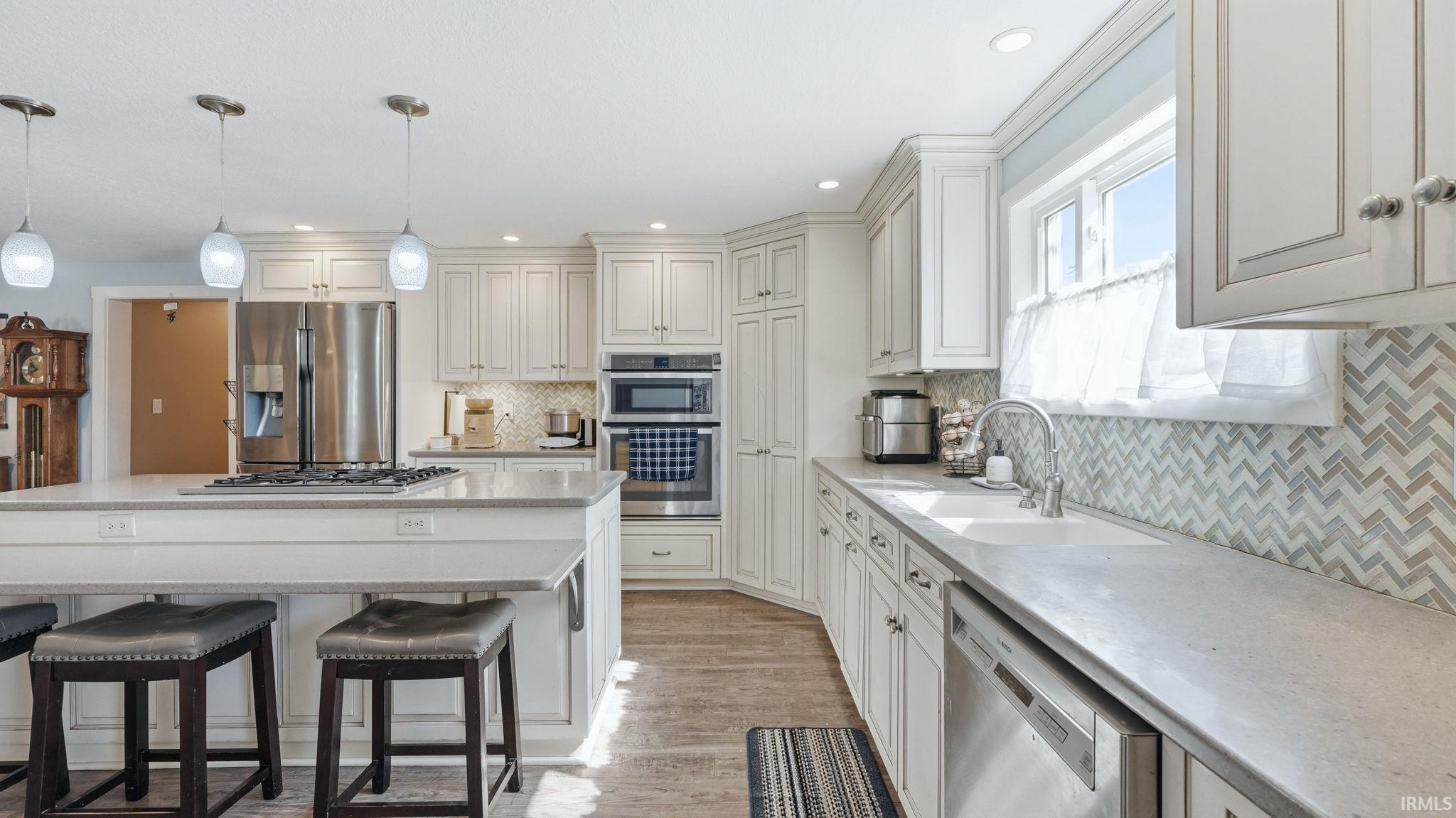 Light-filled kitchen featuring white cabinetry with brushed nickel hardware, light-toned countertops, a herringbone tile backsplash, and wood-finish flooring