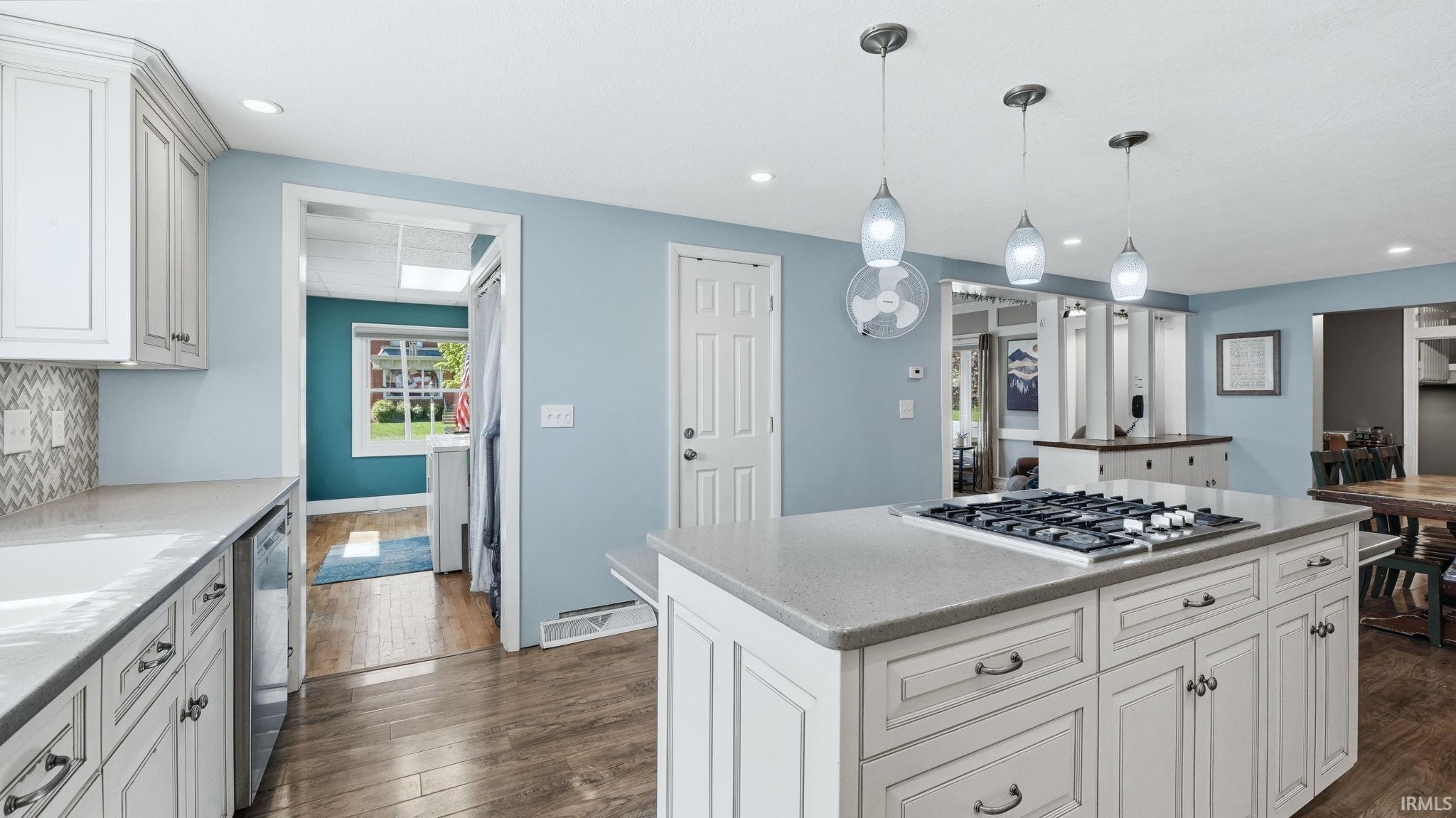 Kitchen featuring an expansive island with a built-in gas cooktop, pendant lighting, white cabinetry, herringbone tile backsplash, and wood-finish flooring