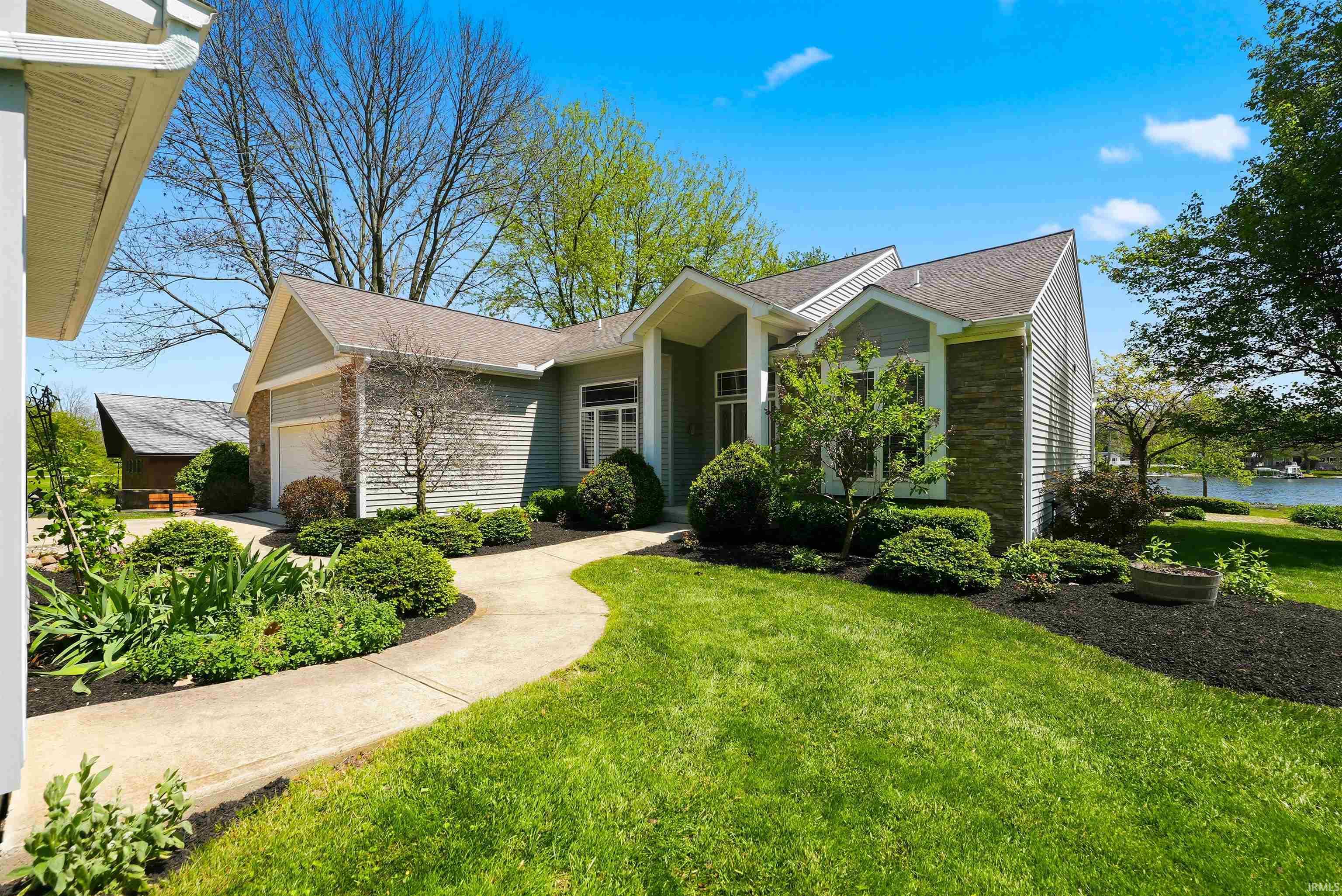 Single-story residence featuring light gray siding with brick accents, an attached garage, and a winding concrete pathway