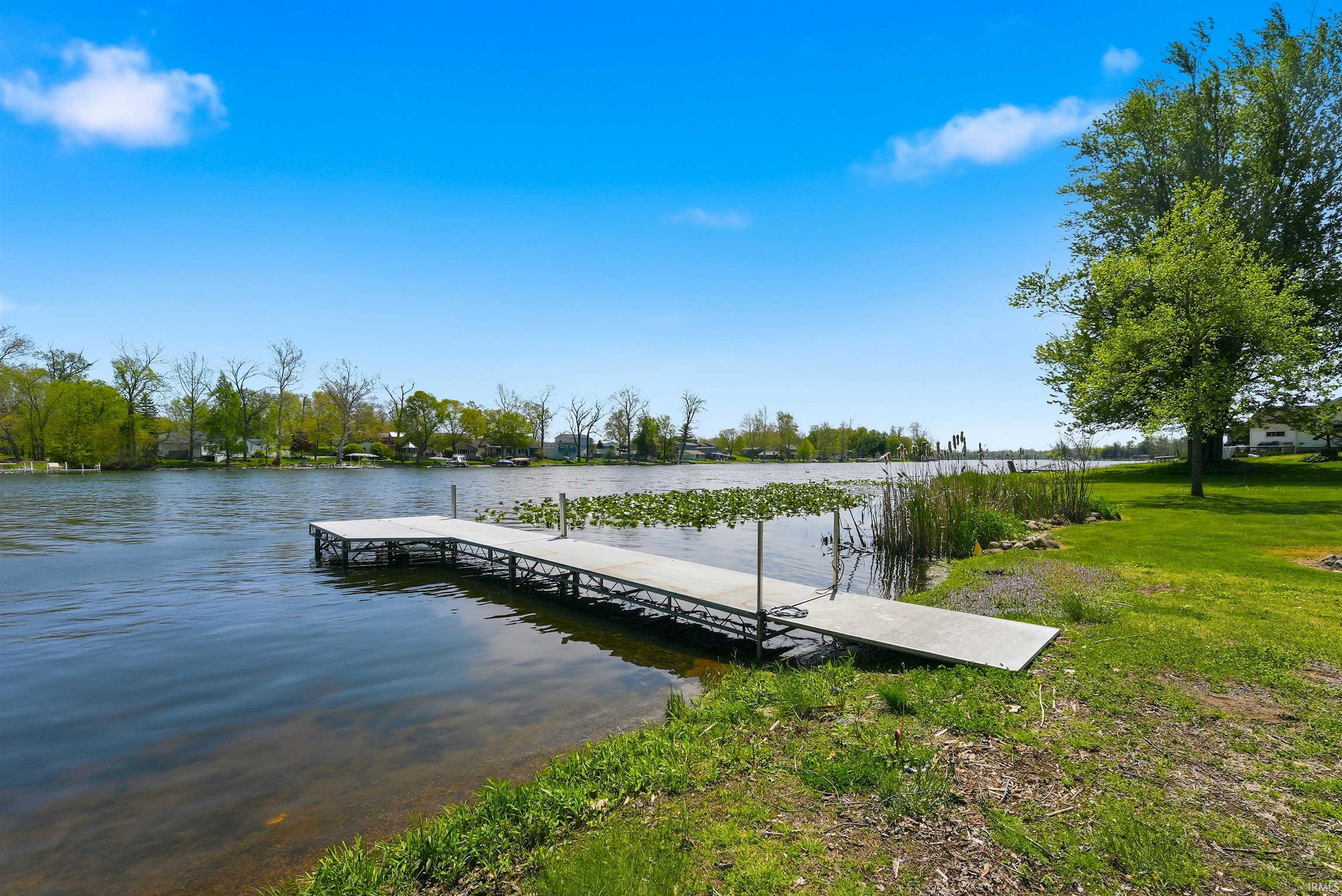 Waterfront property featuring a private dock, green lawn, and mature trees